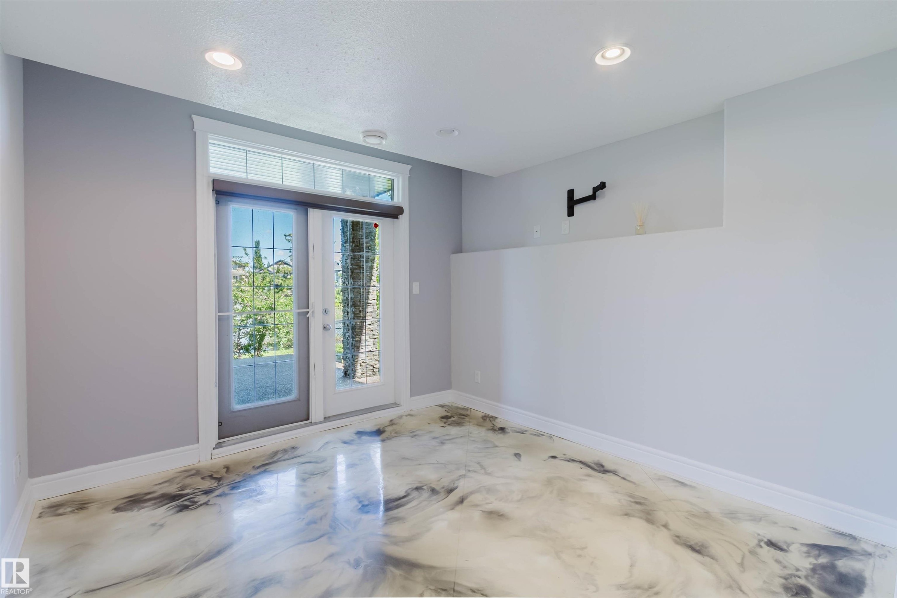 Room featuring unique epoxy flooring, French doors with transom window, recessed lighting, and a partial wall structure - 3438 West Landing Landing, Edmonton, AB
