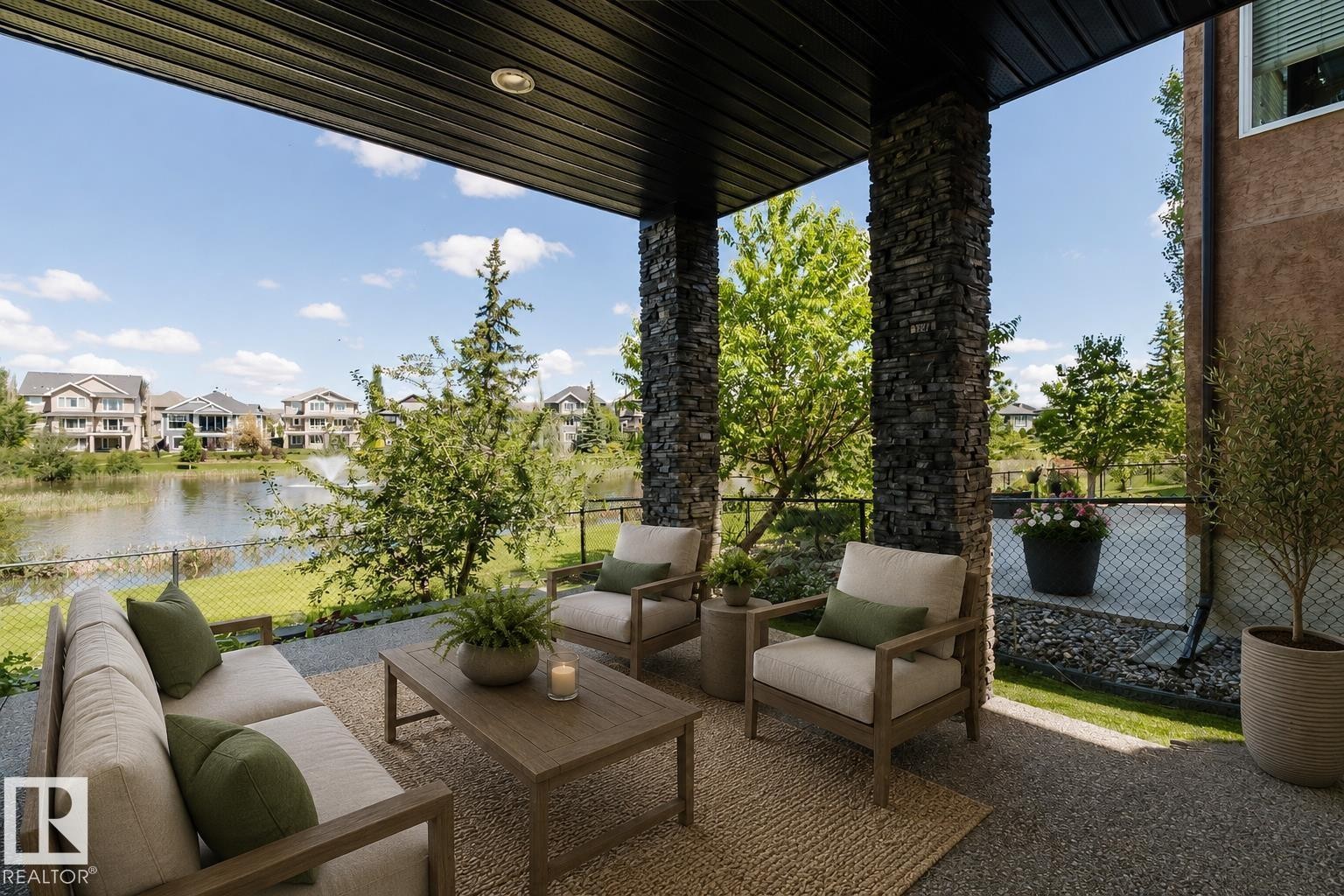 Covered patio featuring stacked stone pillars, recessed lighting, and a durable aggregate surface overlooking a serene pond with a water feature and surrounding residences - 3438 West Landing Landing, Edmonton, AB