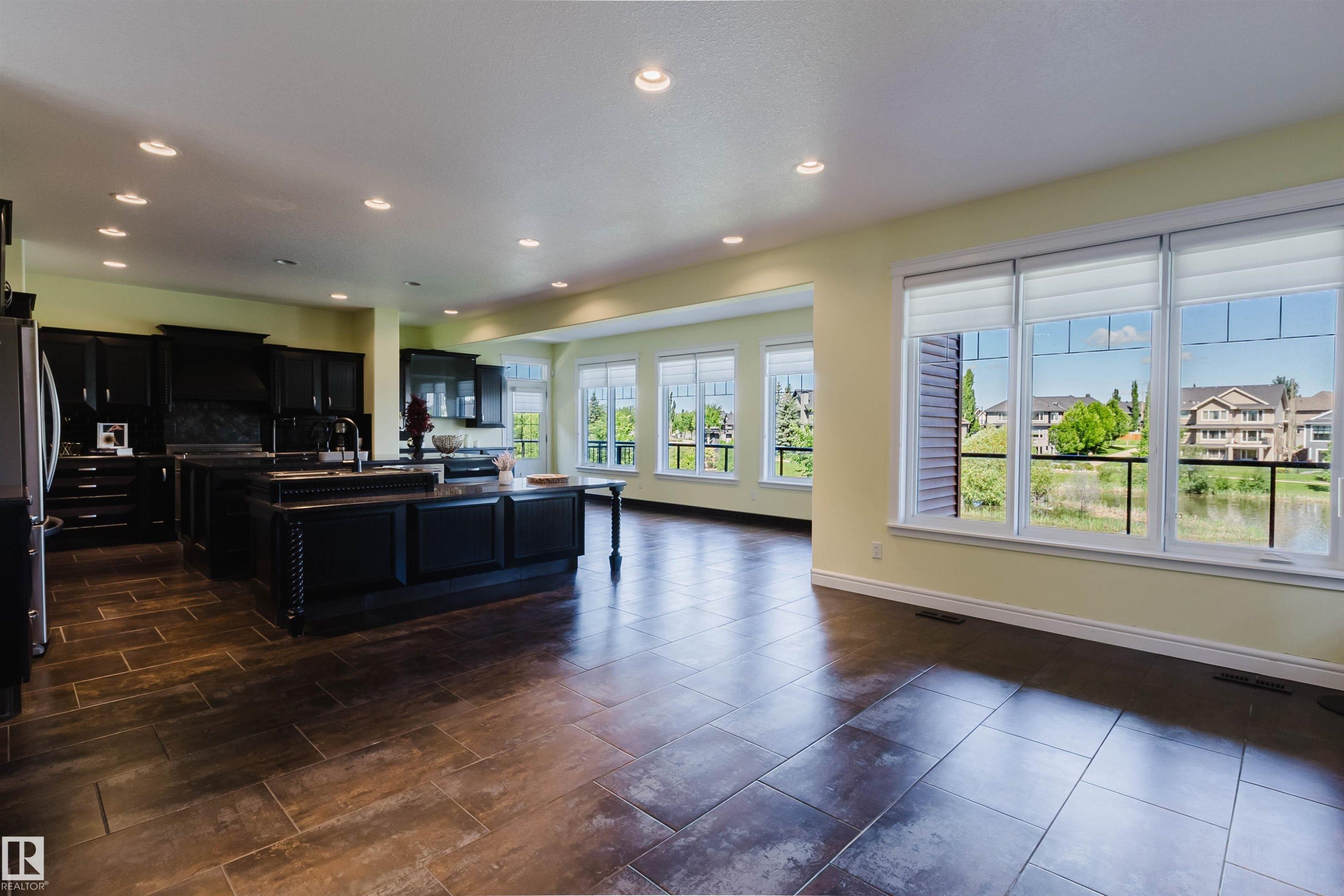 Expansive open-concept living area featuring wood-finish tile flooring, recessed lighting, and a kitchen with dark cabinetry and an island workstation - 3438 West Landing Landing, Edmonton, AB