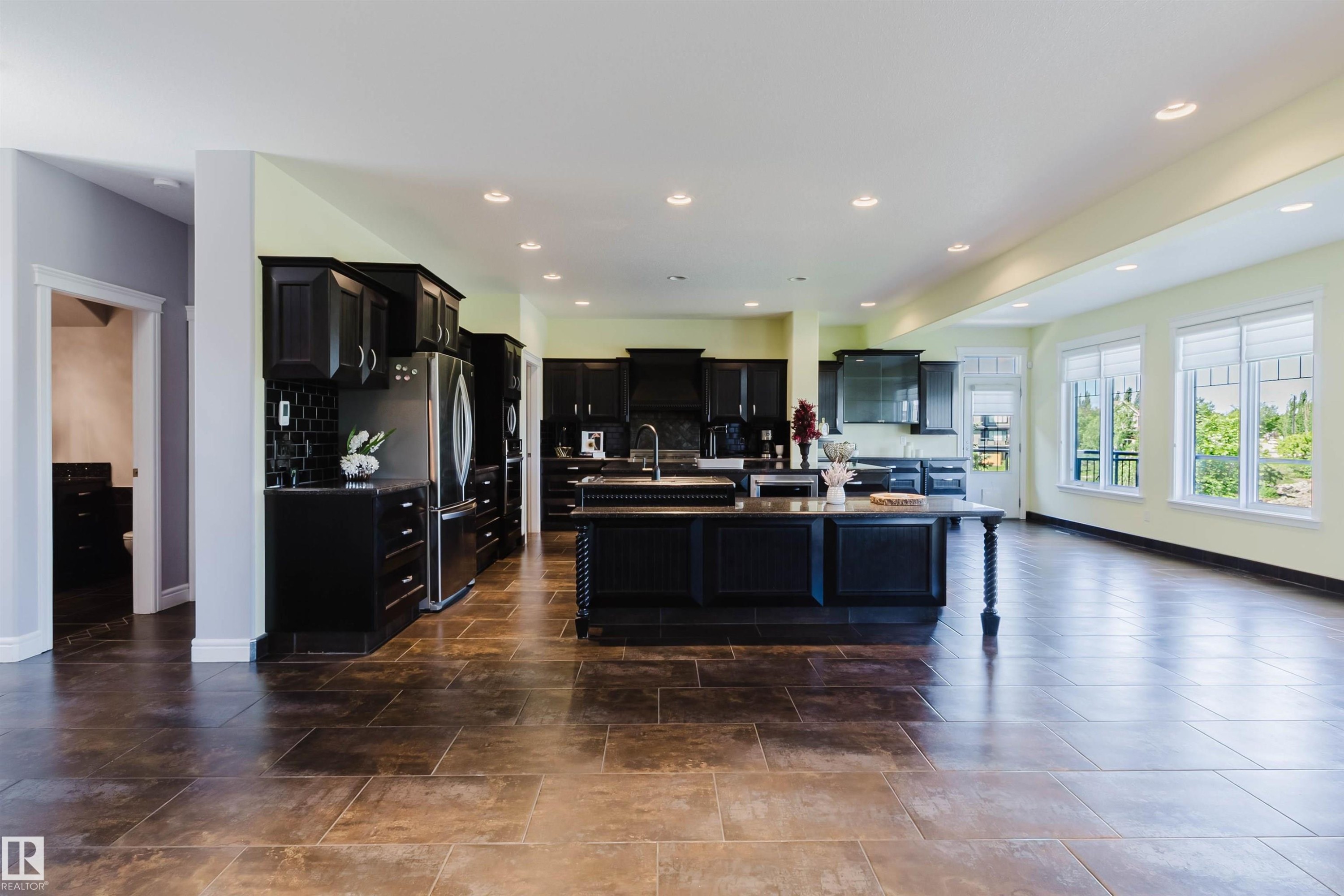 Open-concept kitchen and living area featuring dark wood cabinetry, a large kitchen island with turned legs, stainless steel appliances, and tiled flooring - 3438 West Landing Landing, Edmonton, AB