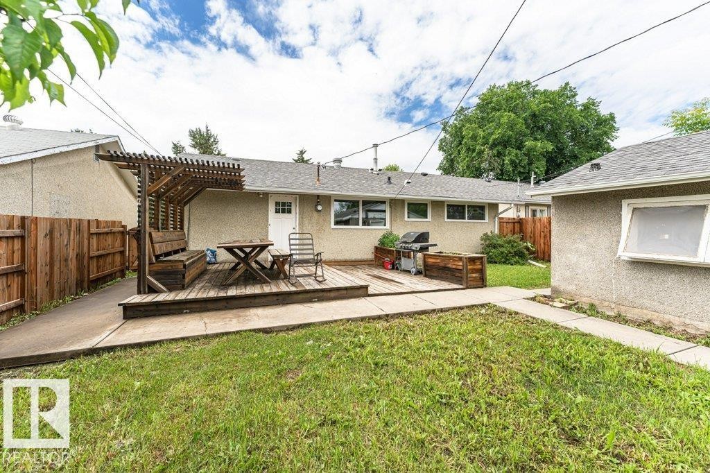 Expansive backyard with a wooden deck featuring a built-in pergola and bench seating - 13411 140 Street, Edmonton, AB