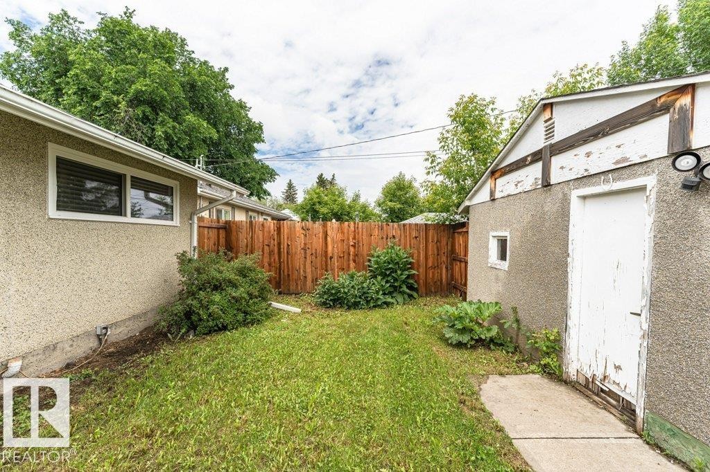 Expansive grassy area featuring a wood privacy fence, established perimeter shrubs, and concrete walkway - 13411 140 Street, Edmonton, AB
