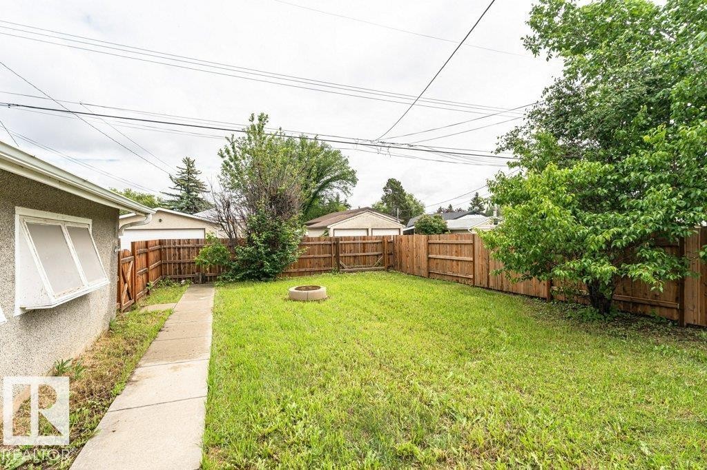 Fenced backyard featuring a manicured lawn, established trees, and a concrete pathway - 13411 140 Street, Edmonton, AB