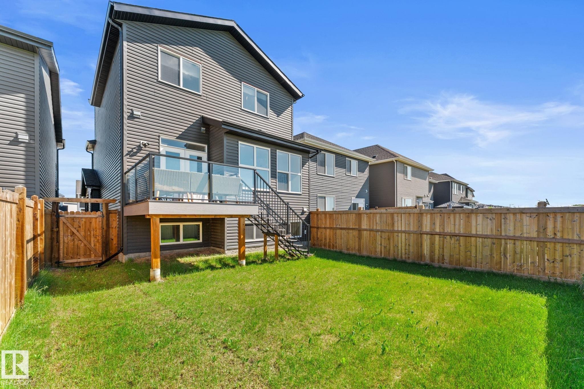 Rear exterior featuring a spacious lawn, wood privacy fencing, and a raised composite deck with glass panel railings - 19 Sturtz Place, Leduc, AB