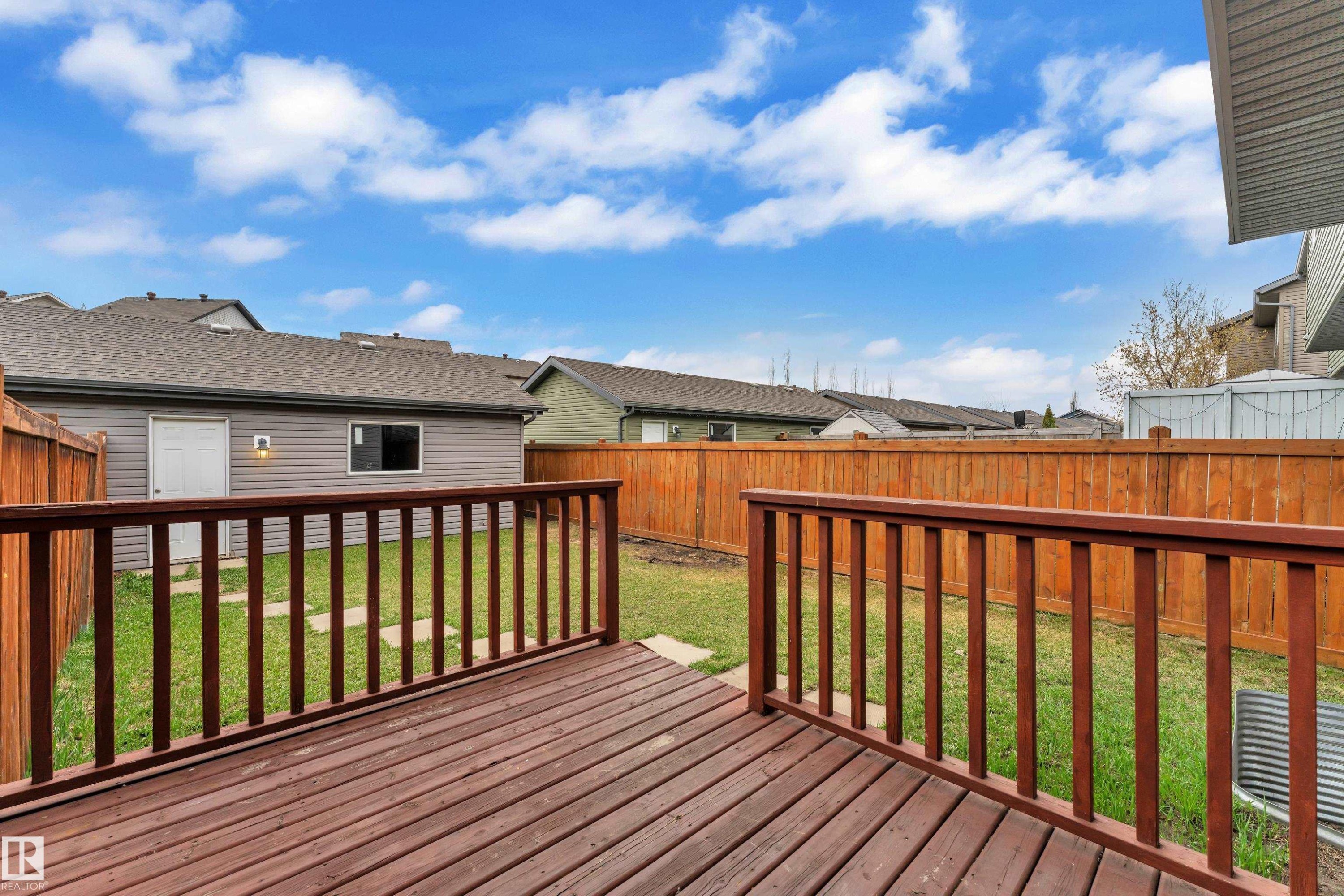 Spacious backyard featuring a wood deck with railings, a manicured lawn, and privacy fencing - 2143 32 Street, Edmonton, AB