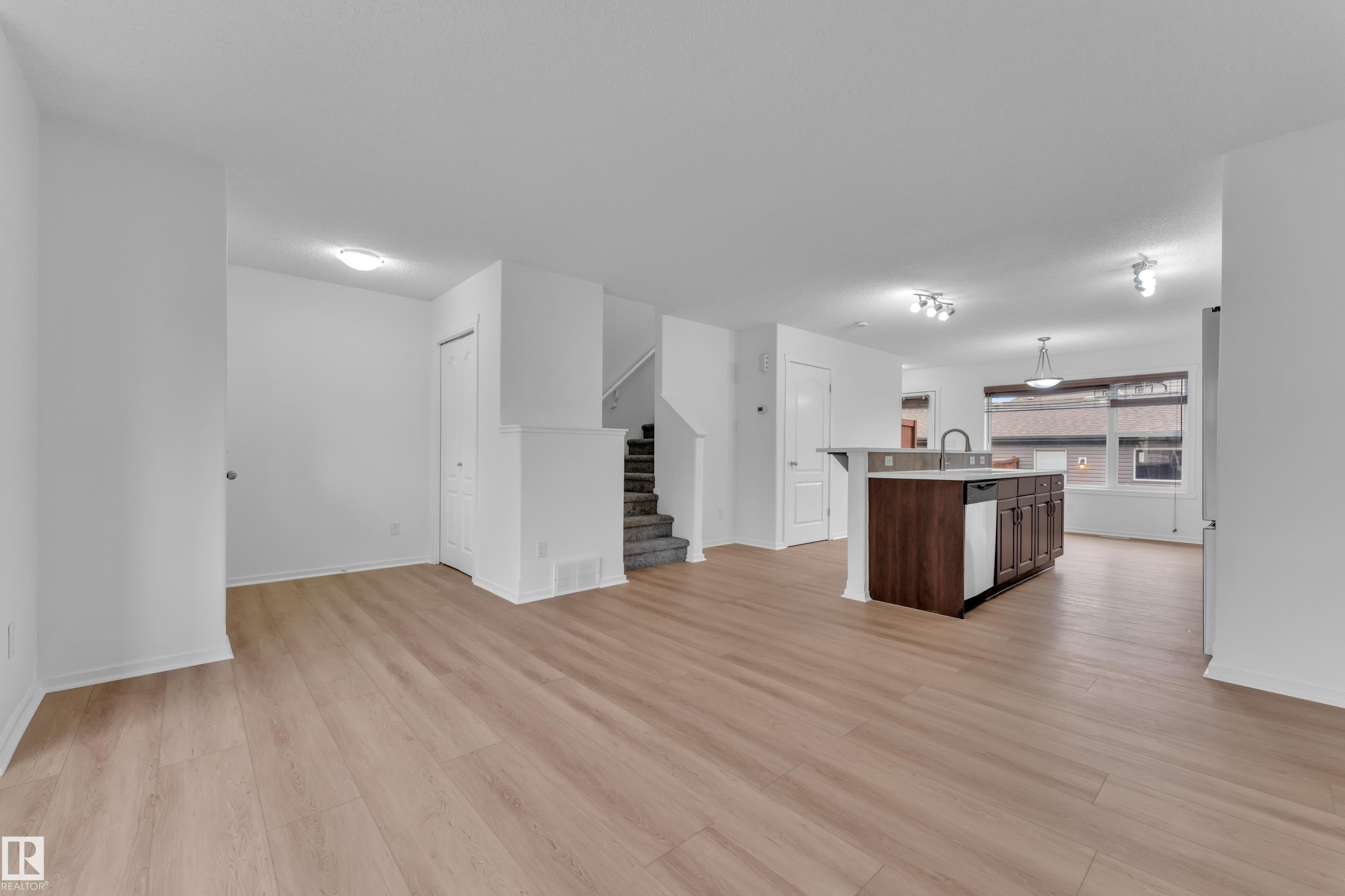 Open-concept main level featuring wood-finish flooring, a kitchen island with integrated sink, stainless steel dishwasher, and track lighting - 2143 32 Street, Edmonton, AB