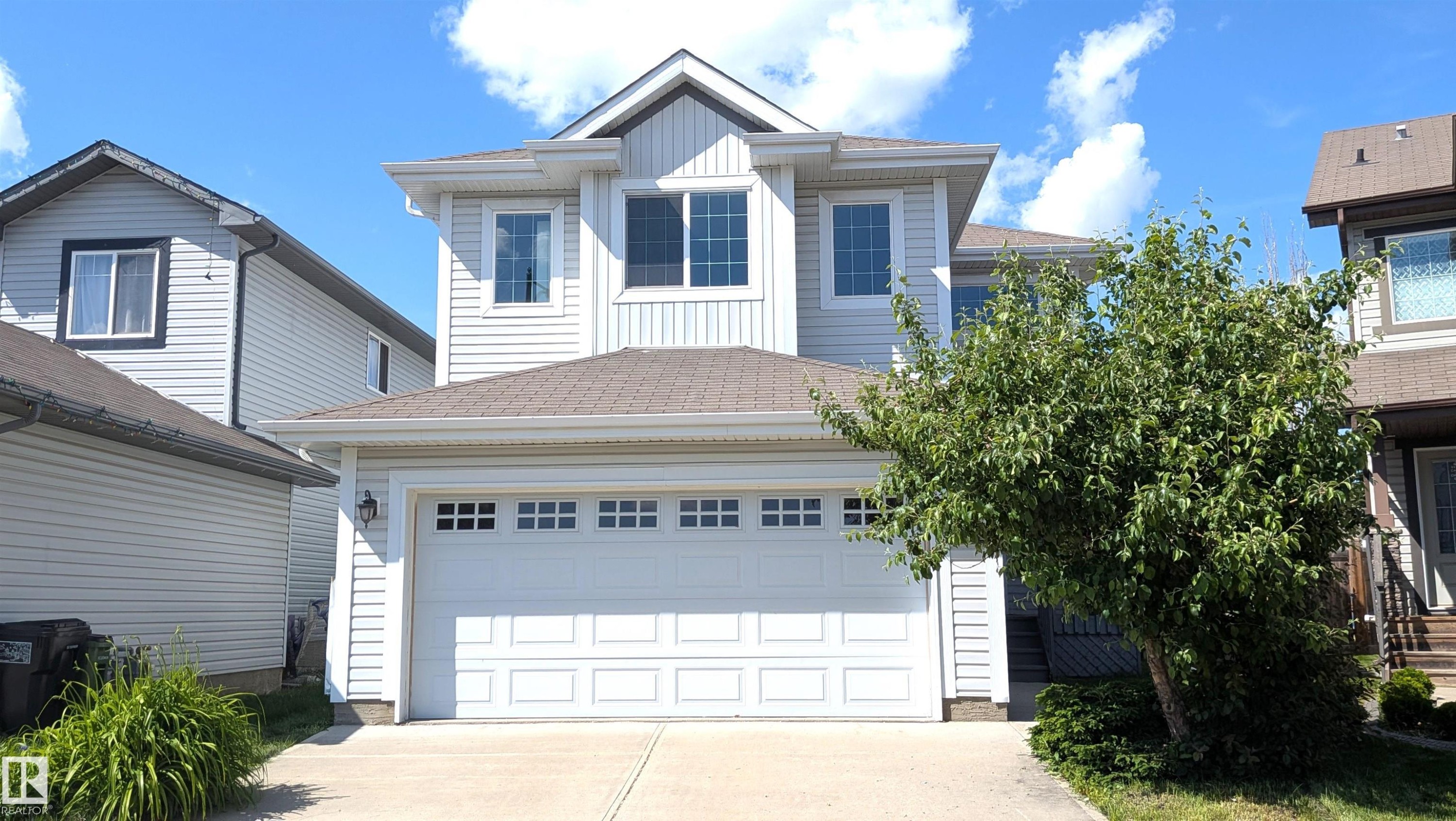 Two-story residence featuring light-colored siding, a prominent two-car garage with window inserts, and multiple upper-level windows - 11312 13 Ave Sw, Edmonton, AB
