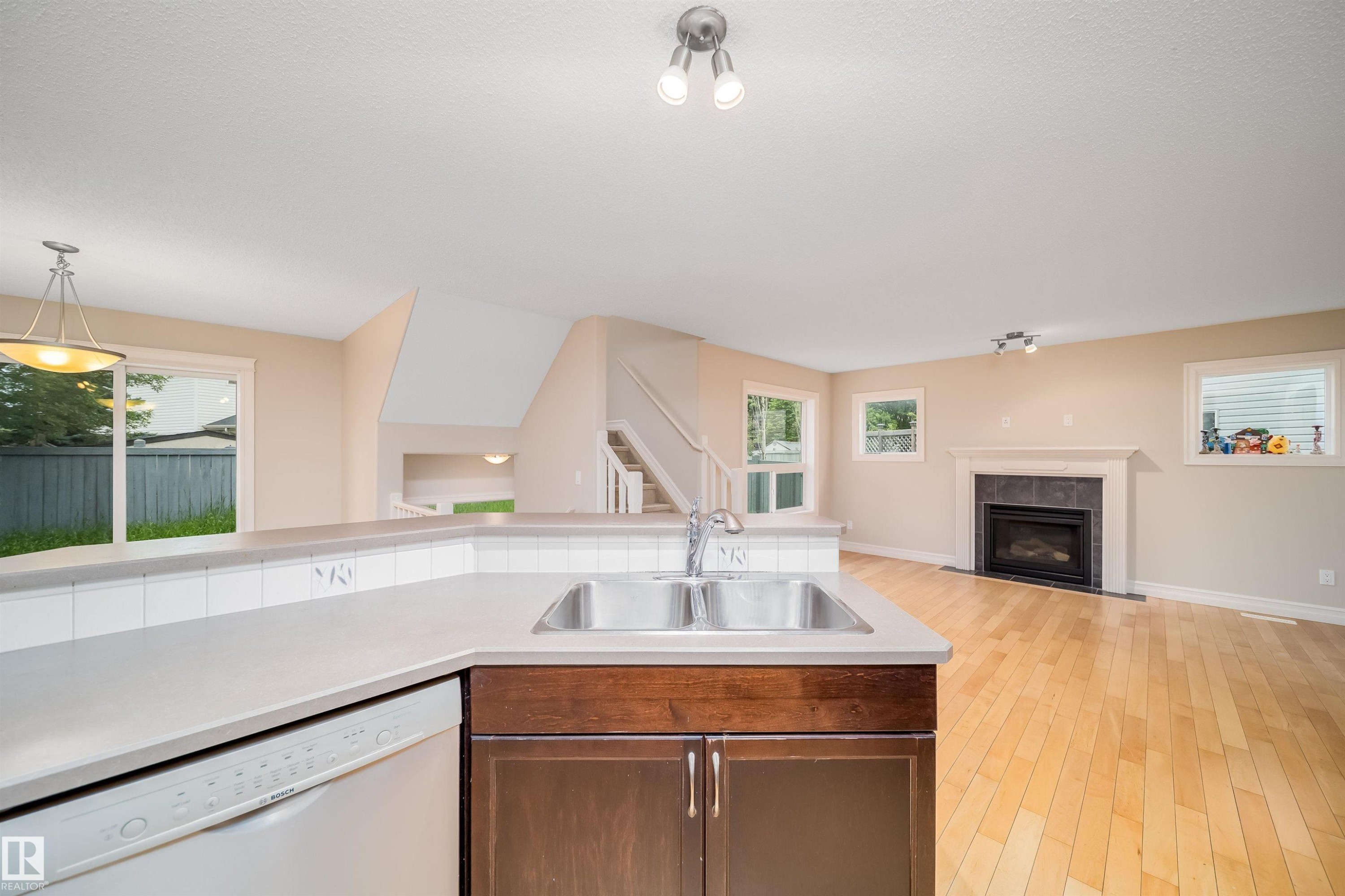 Kitchen counter with integrated double basin sink, white dishwasher, and wood-finish cabinetry - 11312 13 Ave Sw, Edmonton, AB