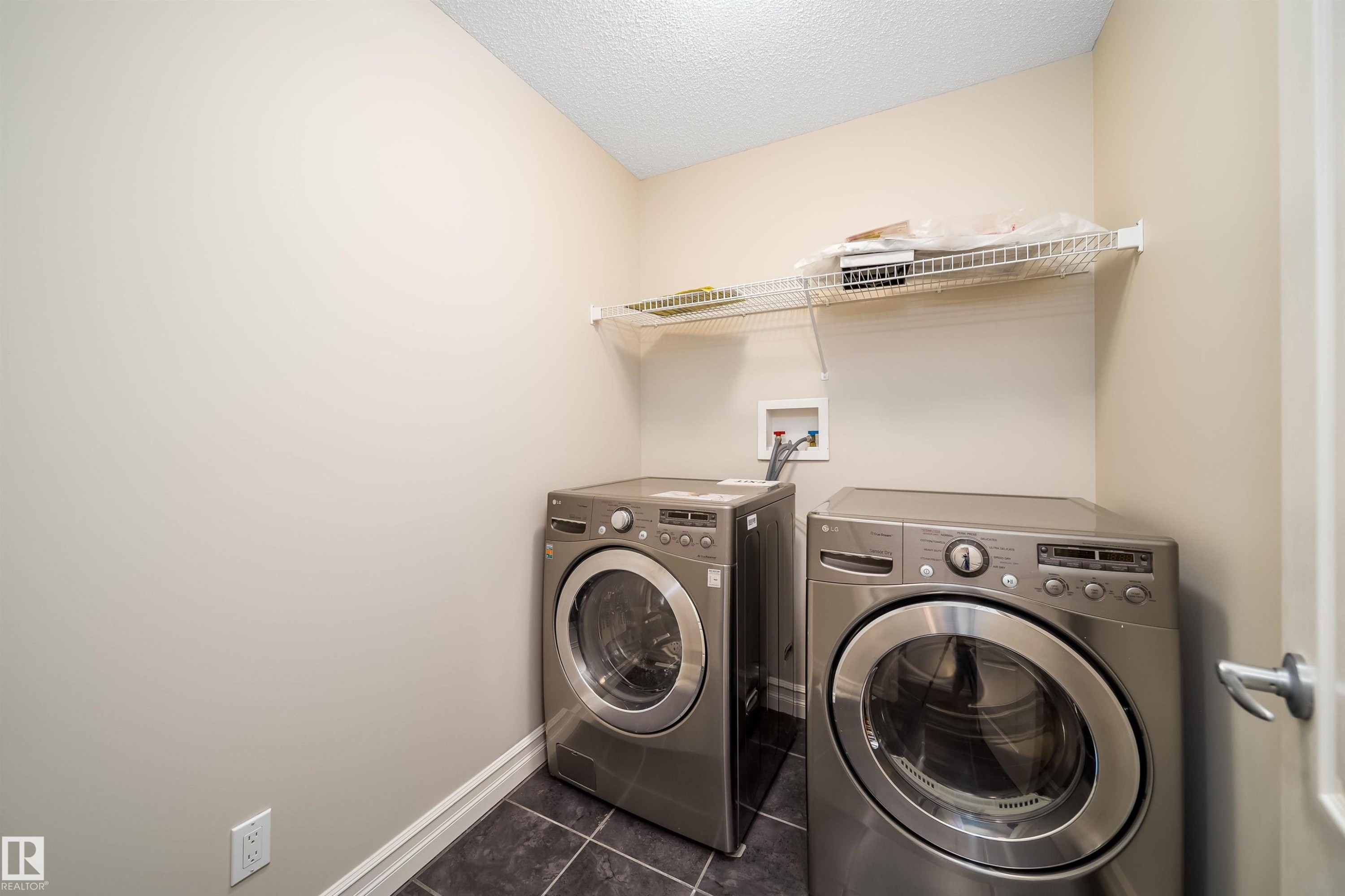 Dedicated laundry area featuring dark tiled flooring, light wall paint, white baseboards, and a wire shelving unit - 11312 13 Ave Sw, Edmonton, AB
