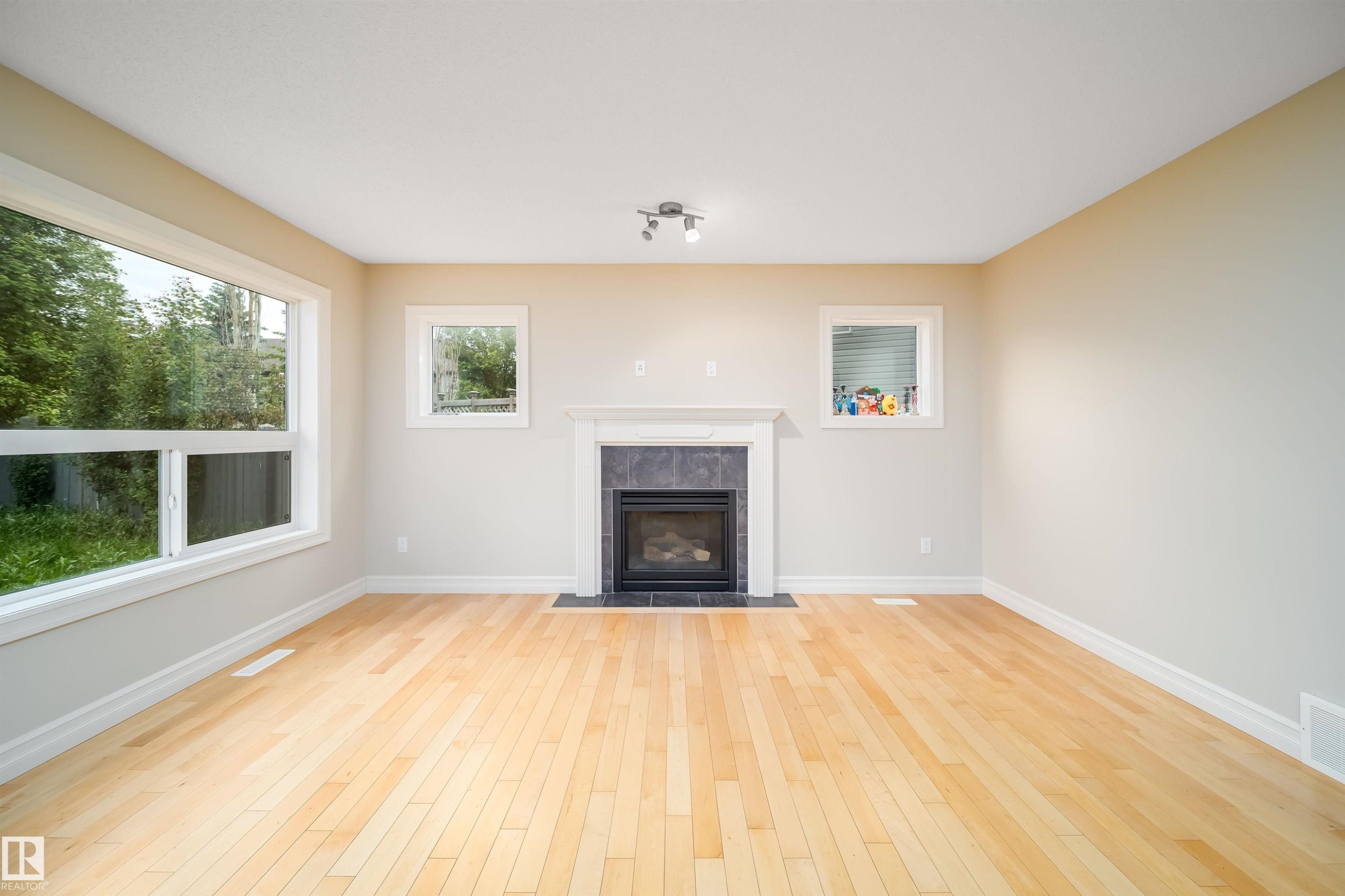 Hardwood flooring throughout a room with a central fireplace featuring a white mantel and dark tile surround - 11312 13 Ave Sw, Edmonton, AB