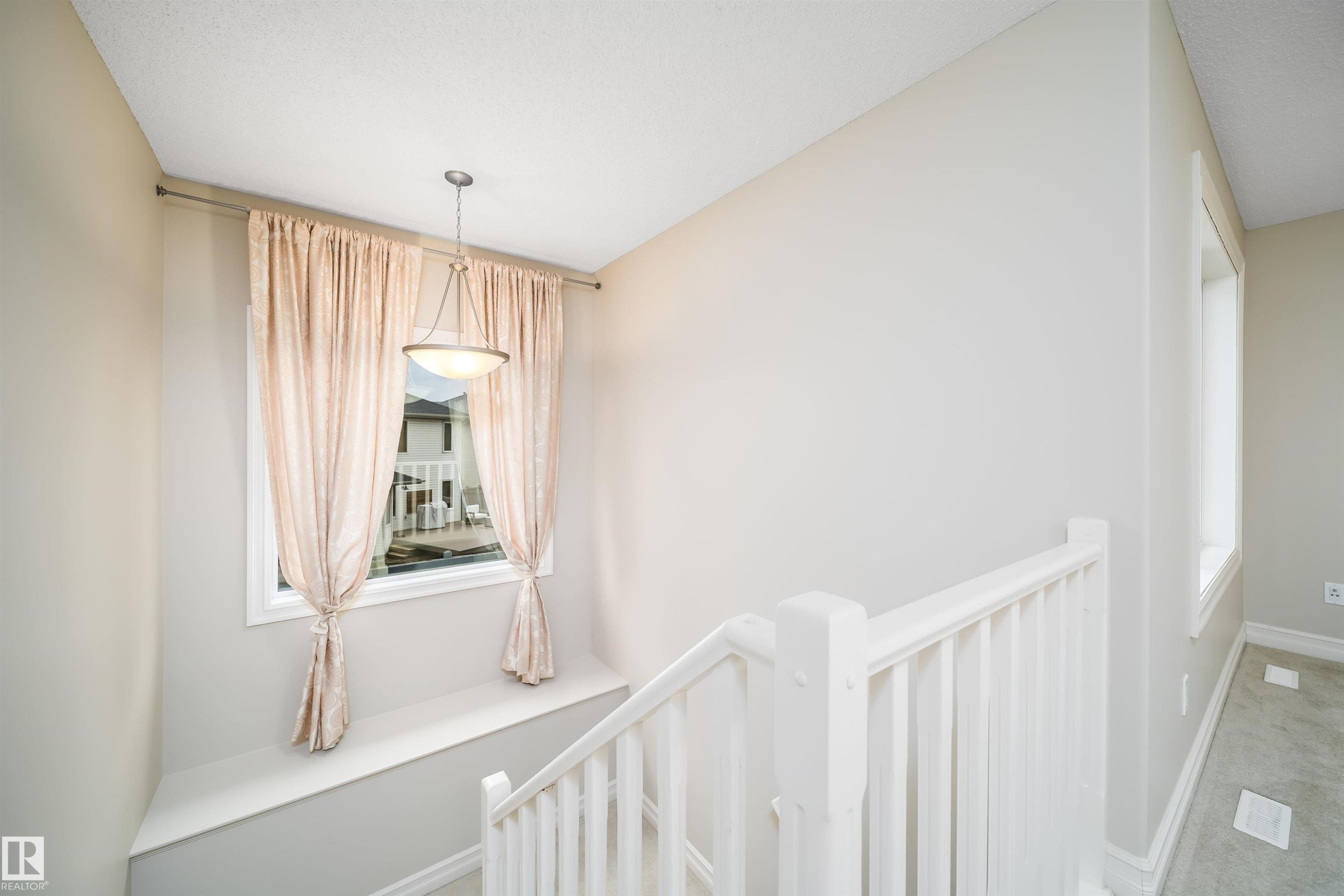 Stairway landing with a window featuring a built-in bench, a suspended ceiling light fixture, and white painted railings - 11312 13 Ave Sw, Edmonton, AB