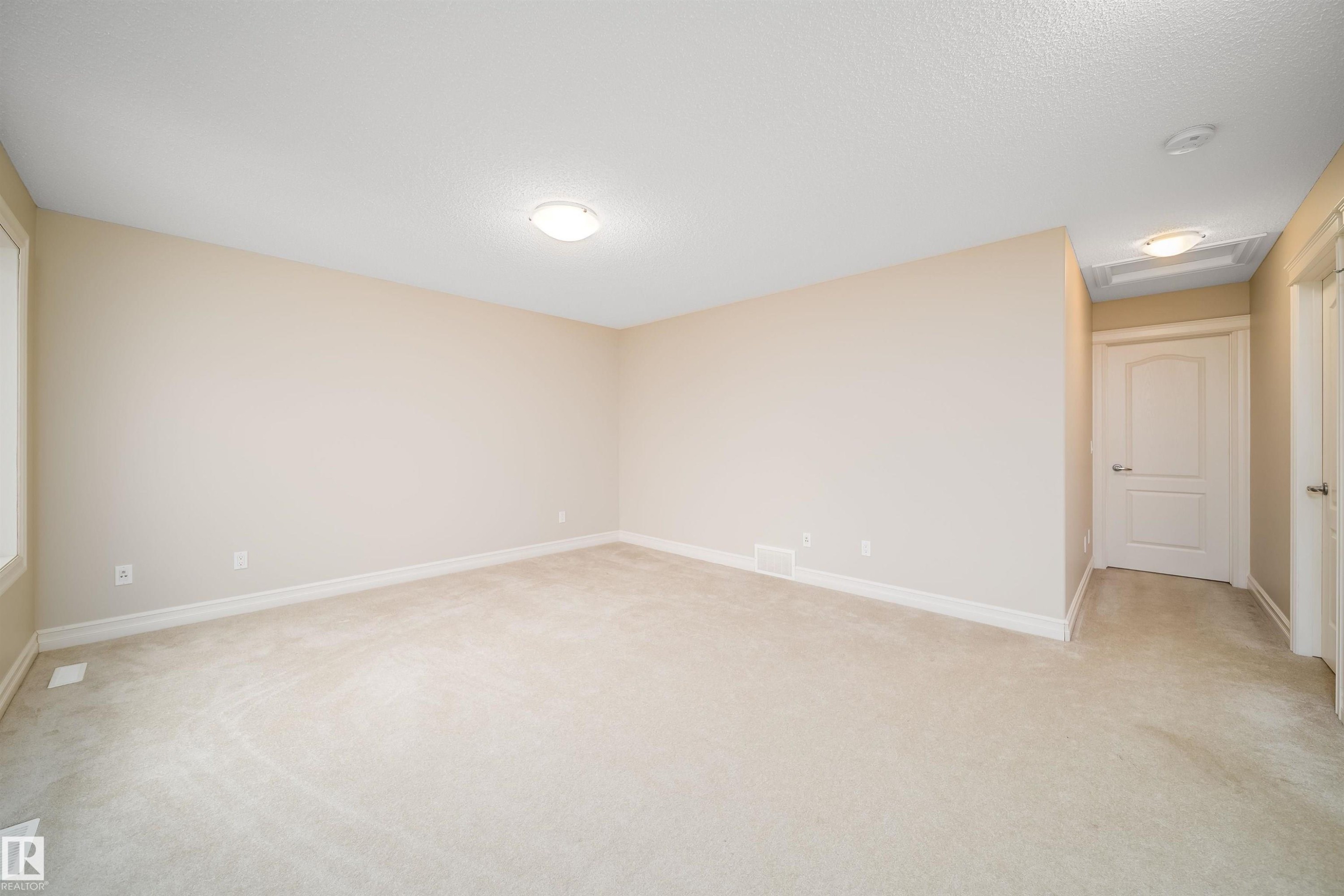 Spacious room featuring neutral carpeting, light-toned walls, and white trim - 11312 13 Ave Sw, Edmonton, AB