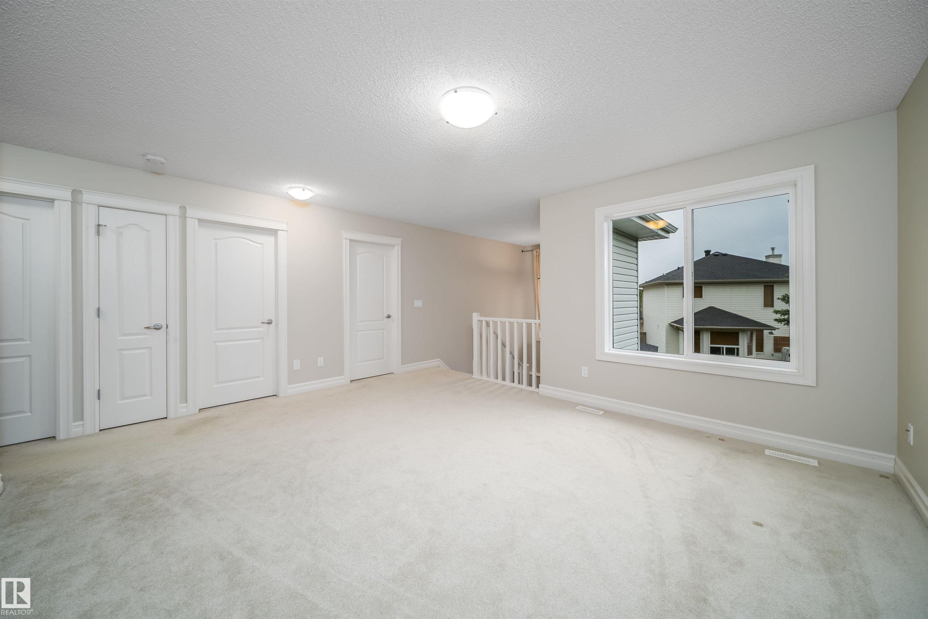 Carpeted room featuring multiple panel doors, white trim, and a prominent window - 11312 13 Ave Sw, Edmonton, AB