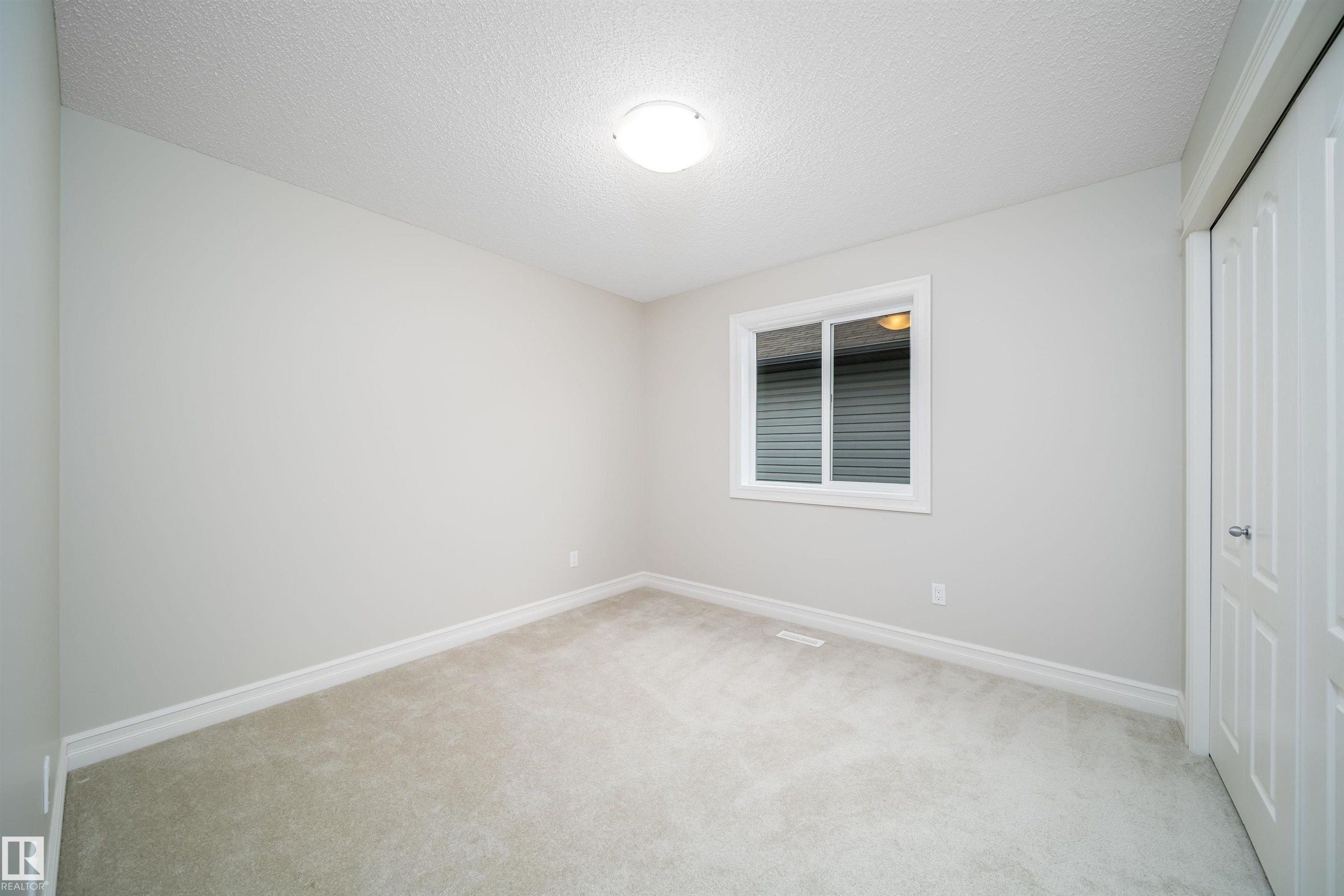 Spacious room featuring neutral carpeting, light gray wall paint, and white trim - 11312 13 Ave Sw, Edmonton, AB