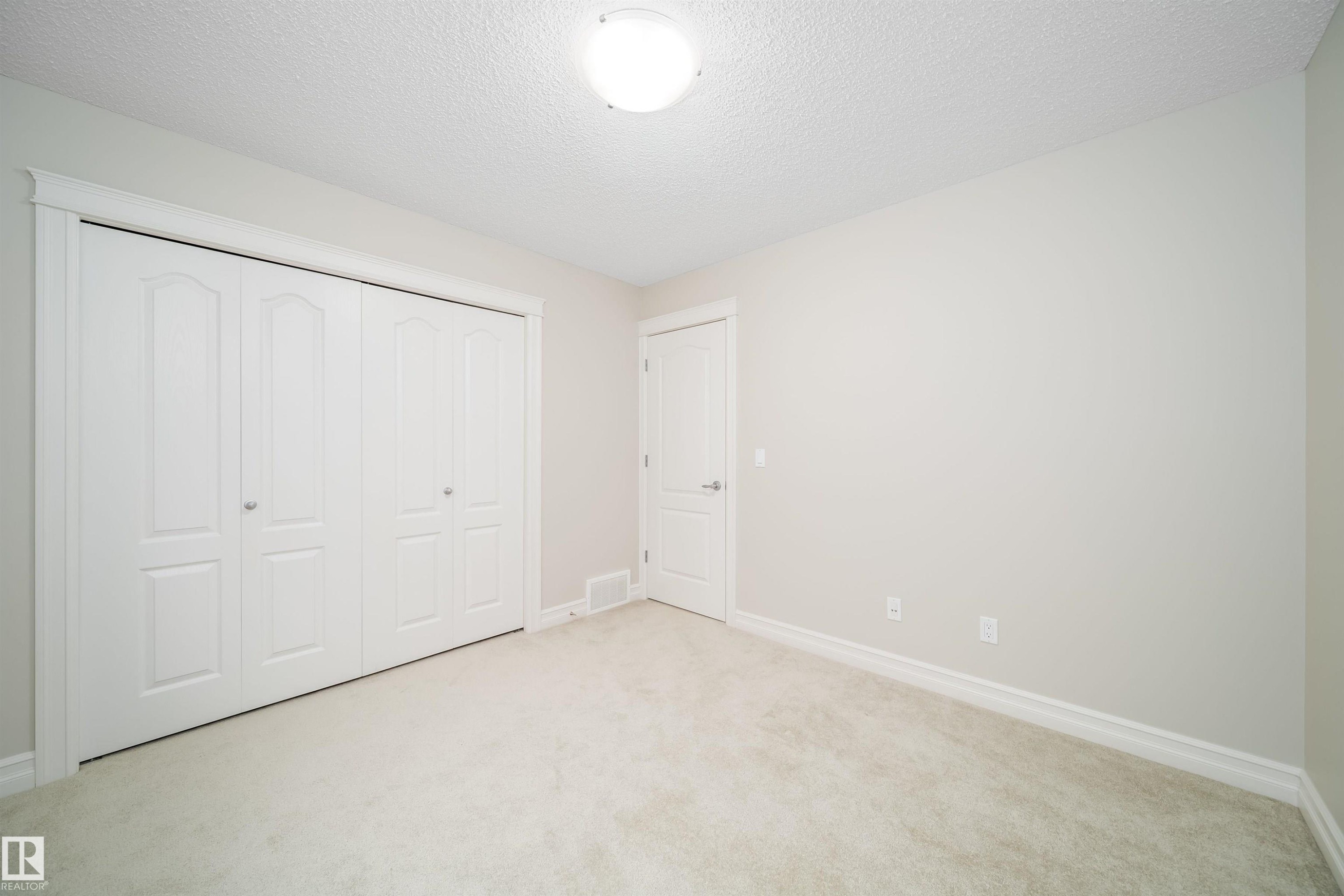 Neutral toned walls, light-colored carpeting, white baseboards, and a bi-fold closet with arched paneling - 11312 13 Ave Sw, Edmonton, AB