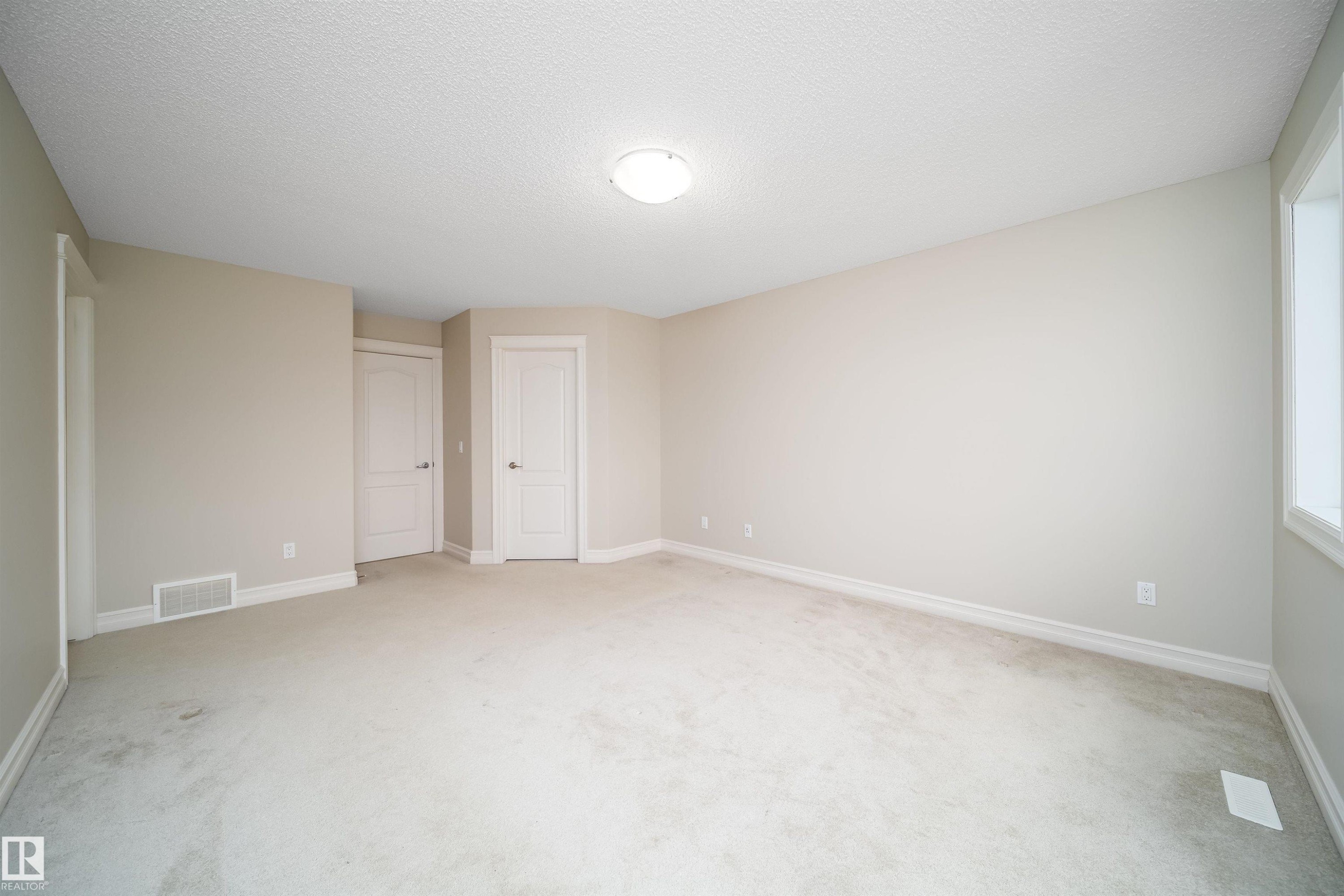 Spacious room featuring neutral carpeting, light-toned wall paint, and white trim molding - 11312 13 Ave Sw, Edmonton, AB