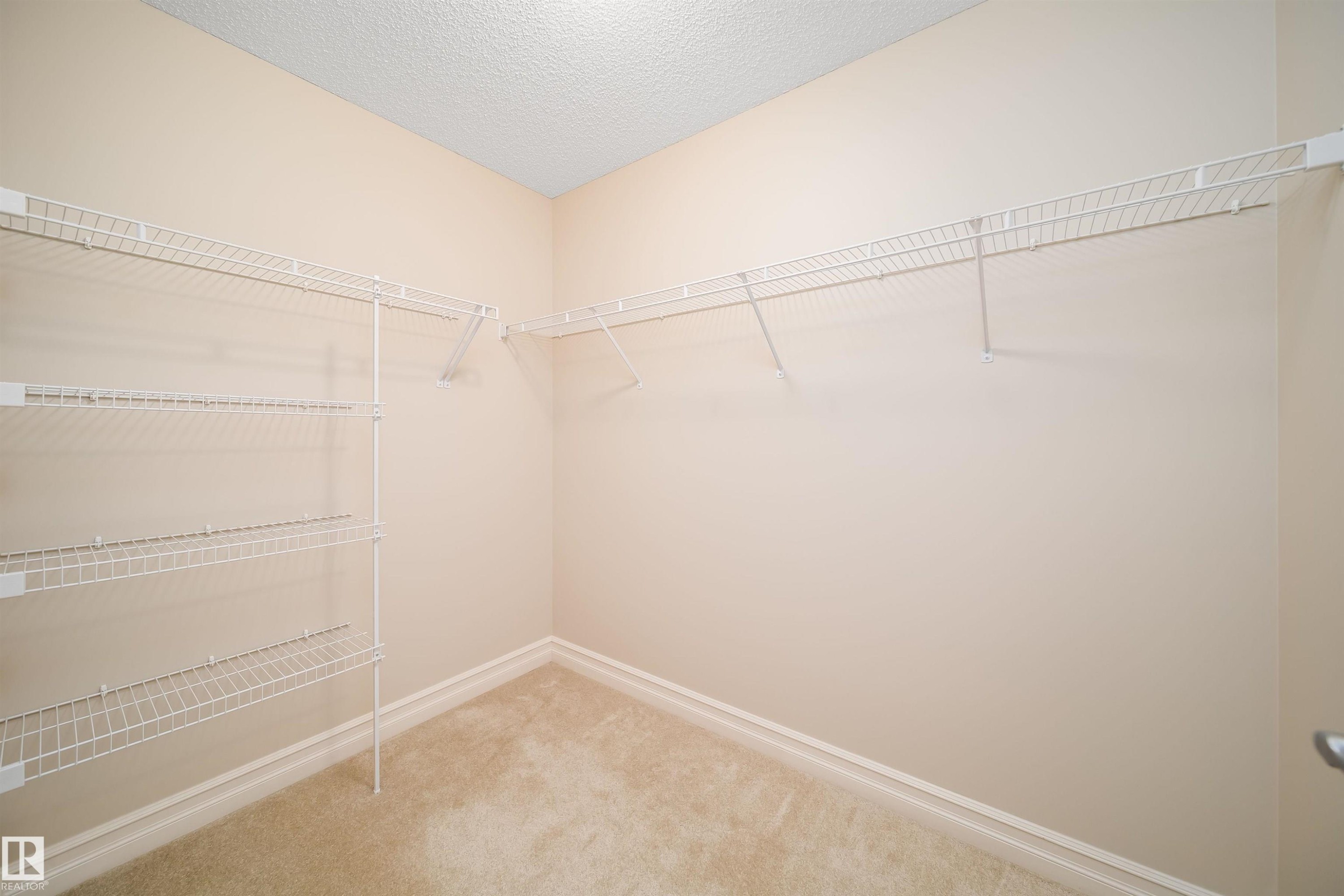 Walk-in closet featuring wire shelving, wire hanging rods, neutral wall paint, textured ceiling, and carpet flooring - 11312 13 Ave Sw, Edmonton, AB