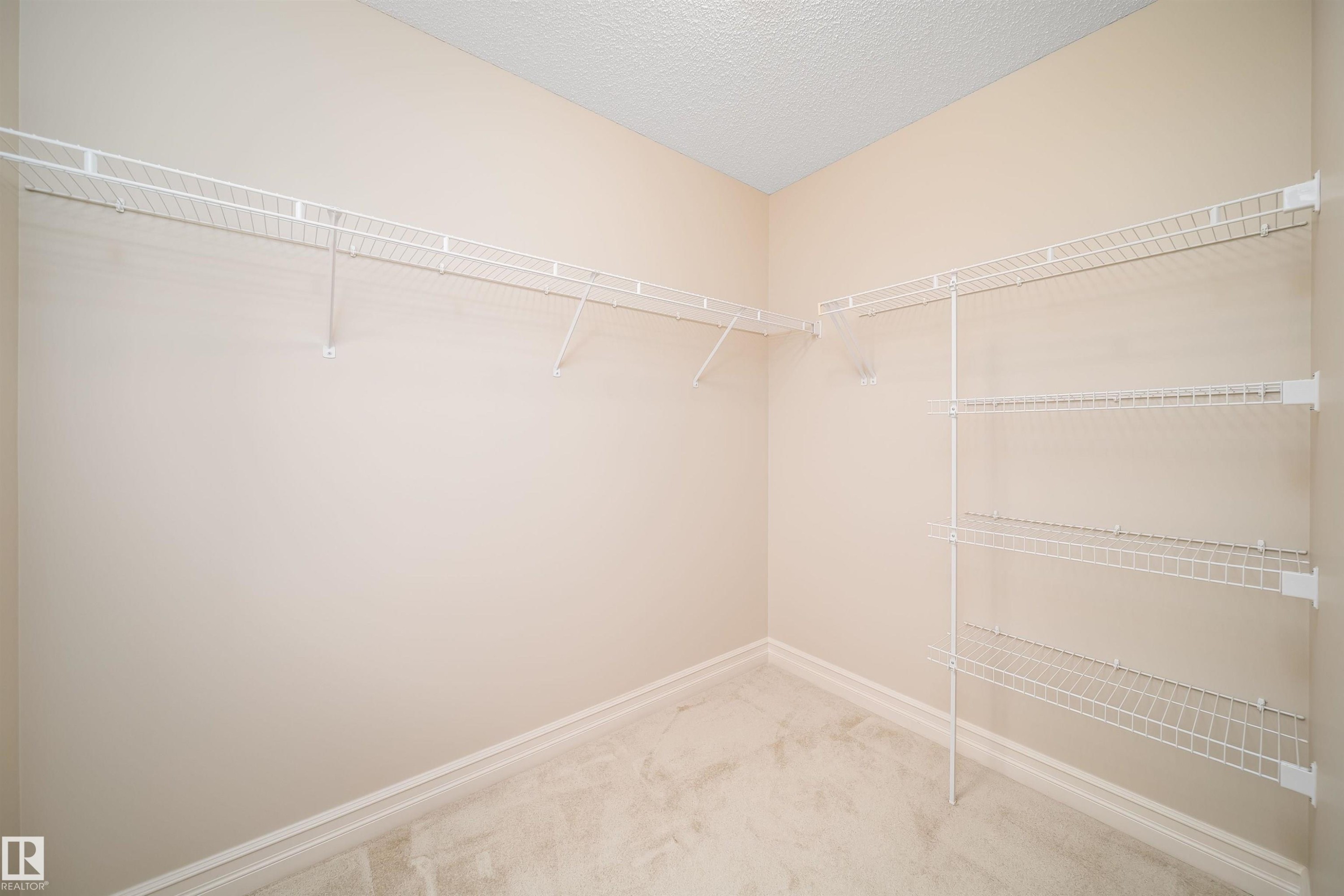 Walk-in closet featuring wire shelving, wire hanging rods, neutral wall paint, white baseboards, and light carpet flooring - 11312 13 Ave Sw, Edmonton, AB