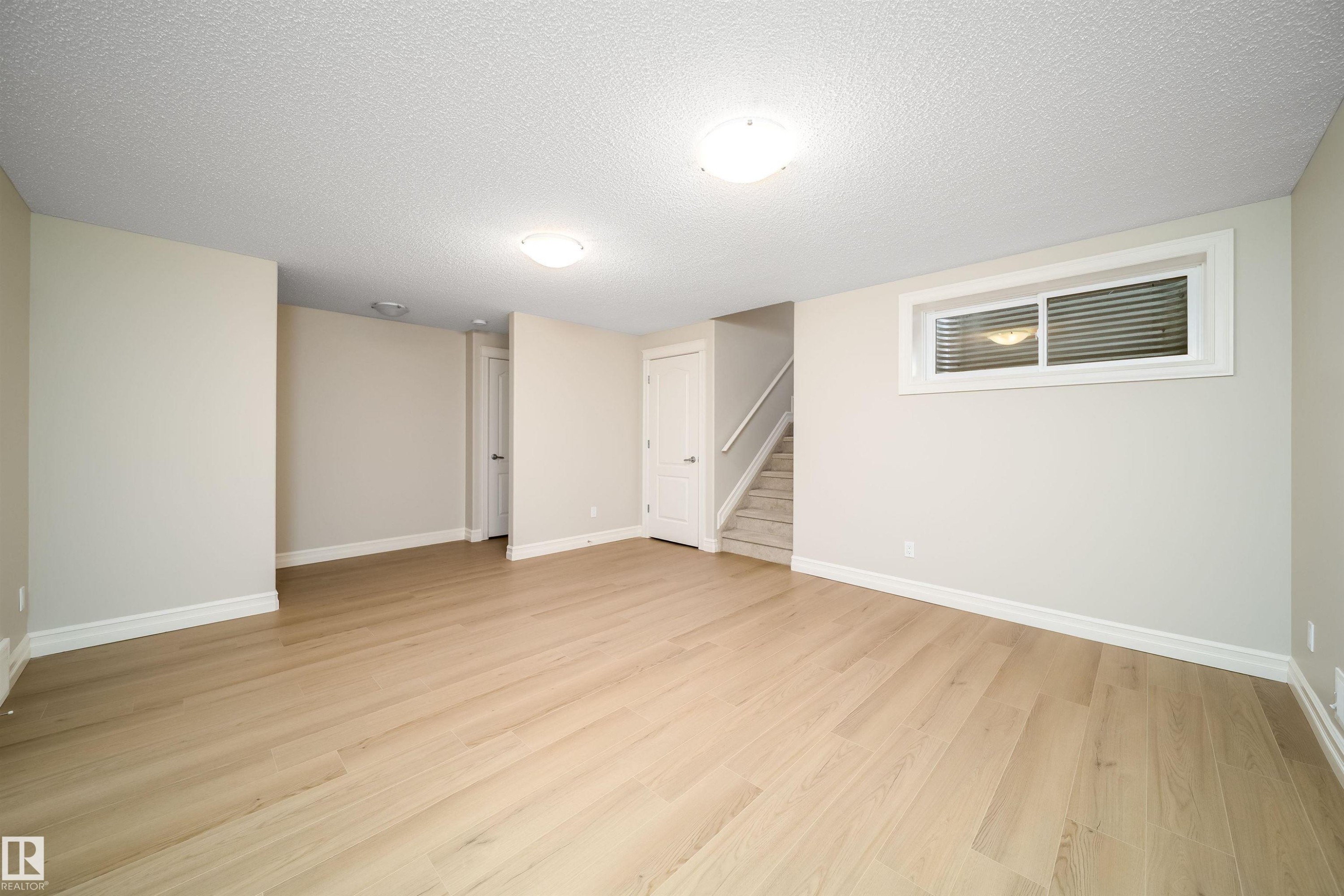 Spacious room featuring wood-finish flooring, neutral-toned walls, and white baseboards - 11312 13 Ave Sw, Edmonton, AB