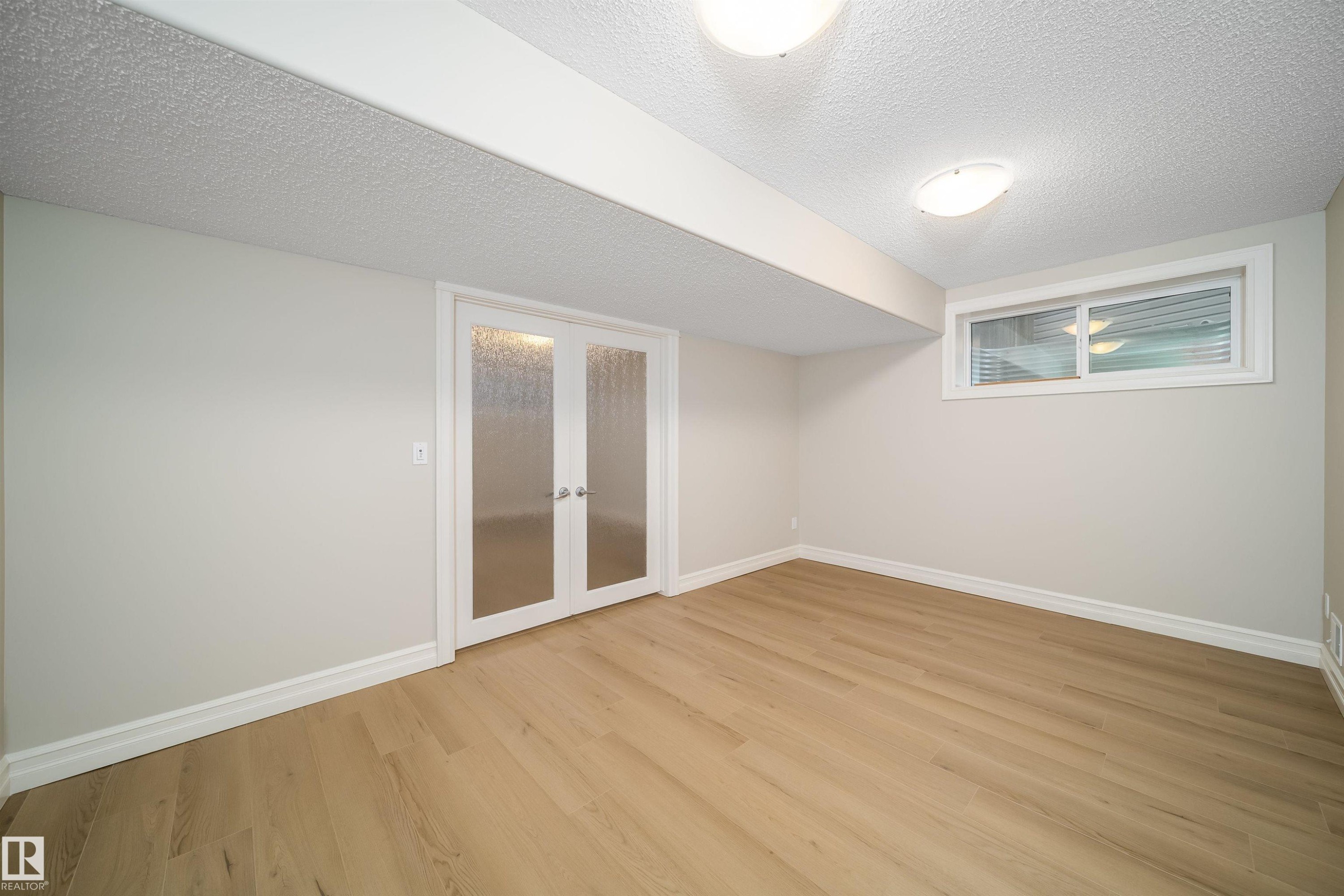 Well-lit room featuring wood-finish flooring, white baseboards, and a neutral wall color - 11312 13 Ave Sw, Edmonton, AB
