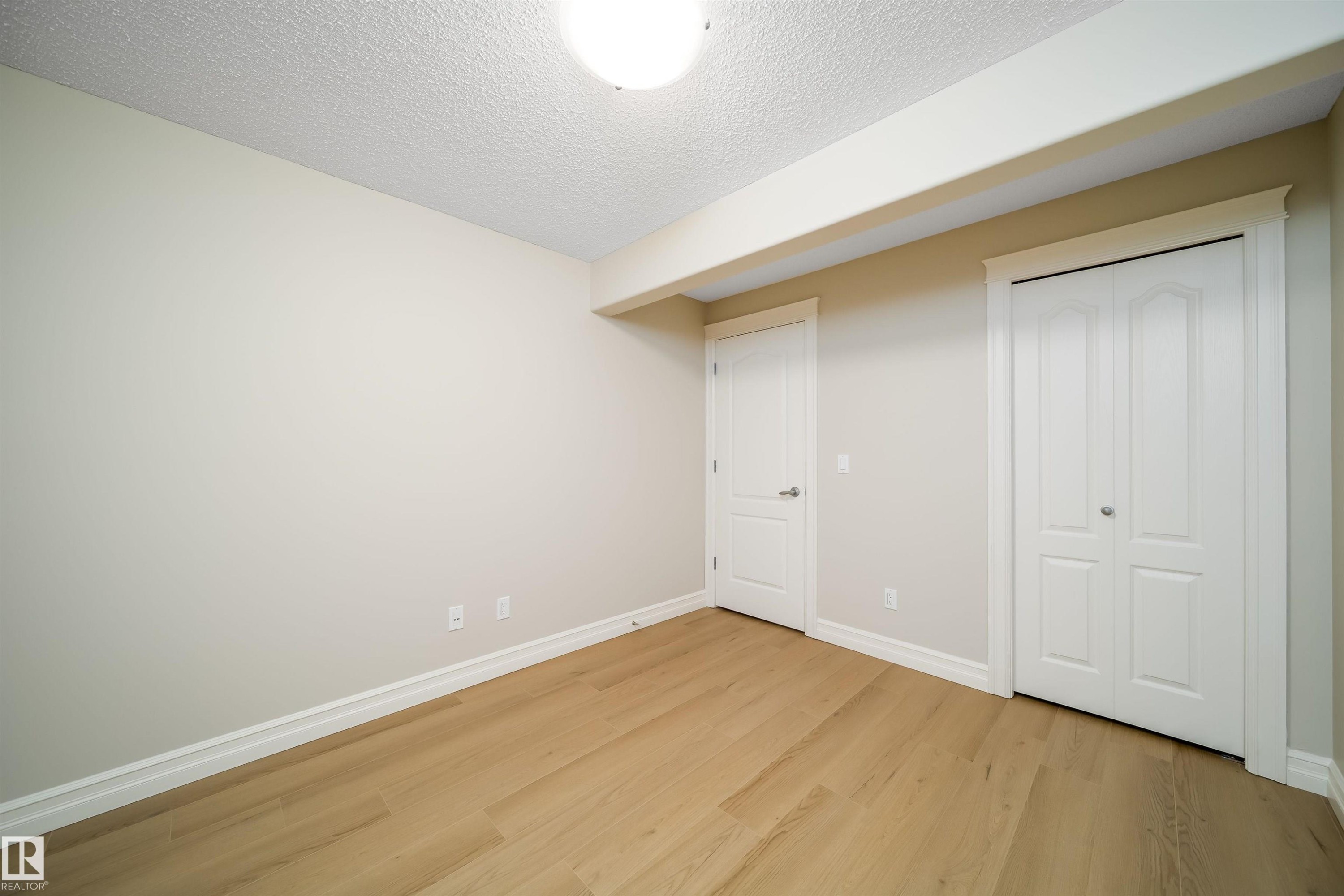 Room featuring wood-finish flooring, neutral wall tones, white trim, and a white ceiling with an overhead light fixture - 11312 13 Ave Sw, Edmonton, AB