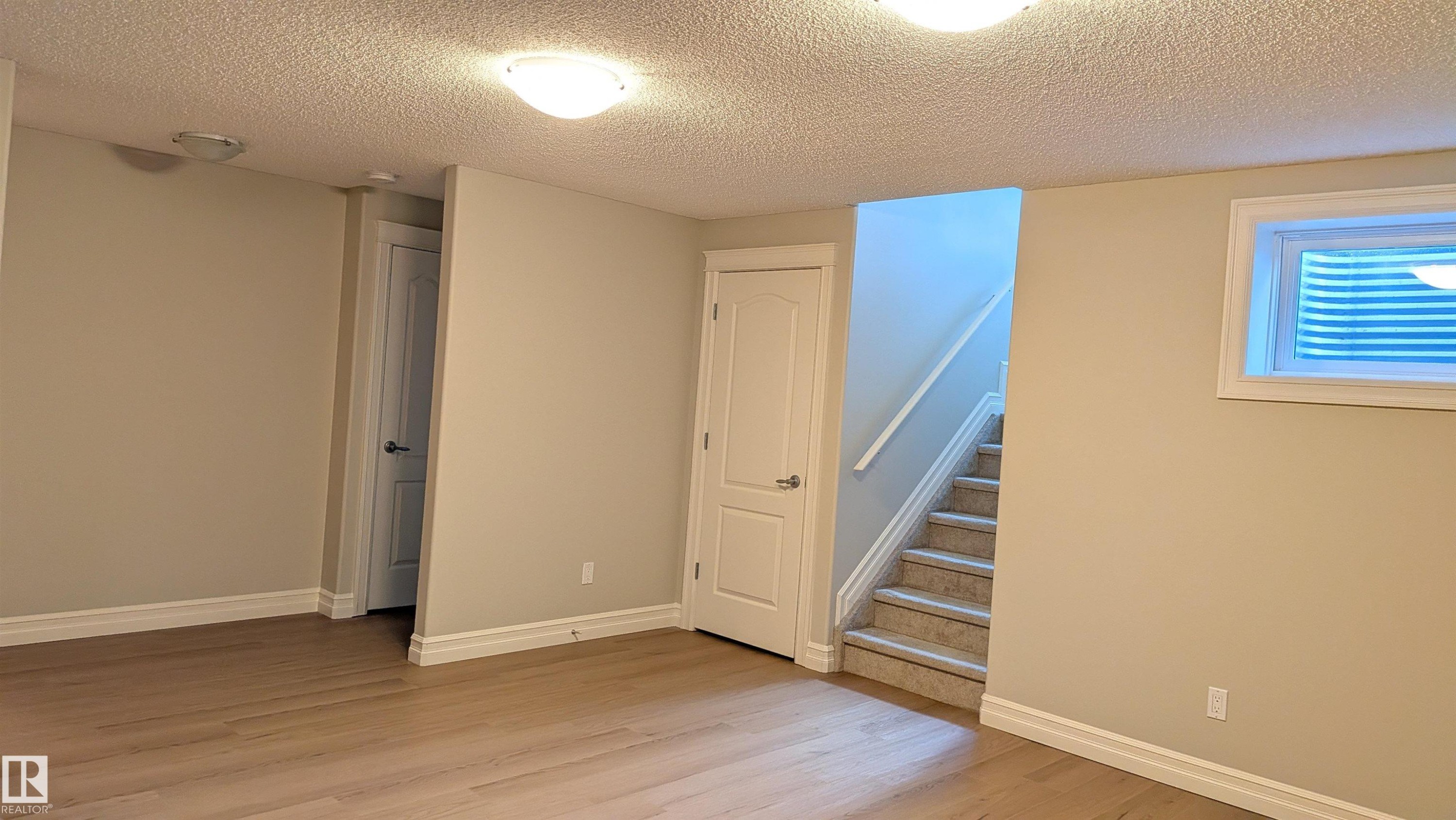 Spacious room featuring wood-finish flooring, light neutral wall paint, and white trim - 11312 13 Ave Sw, Edmonton, AB