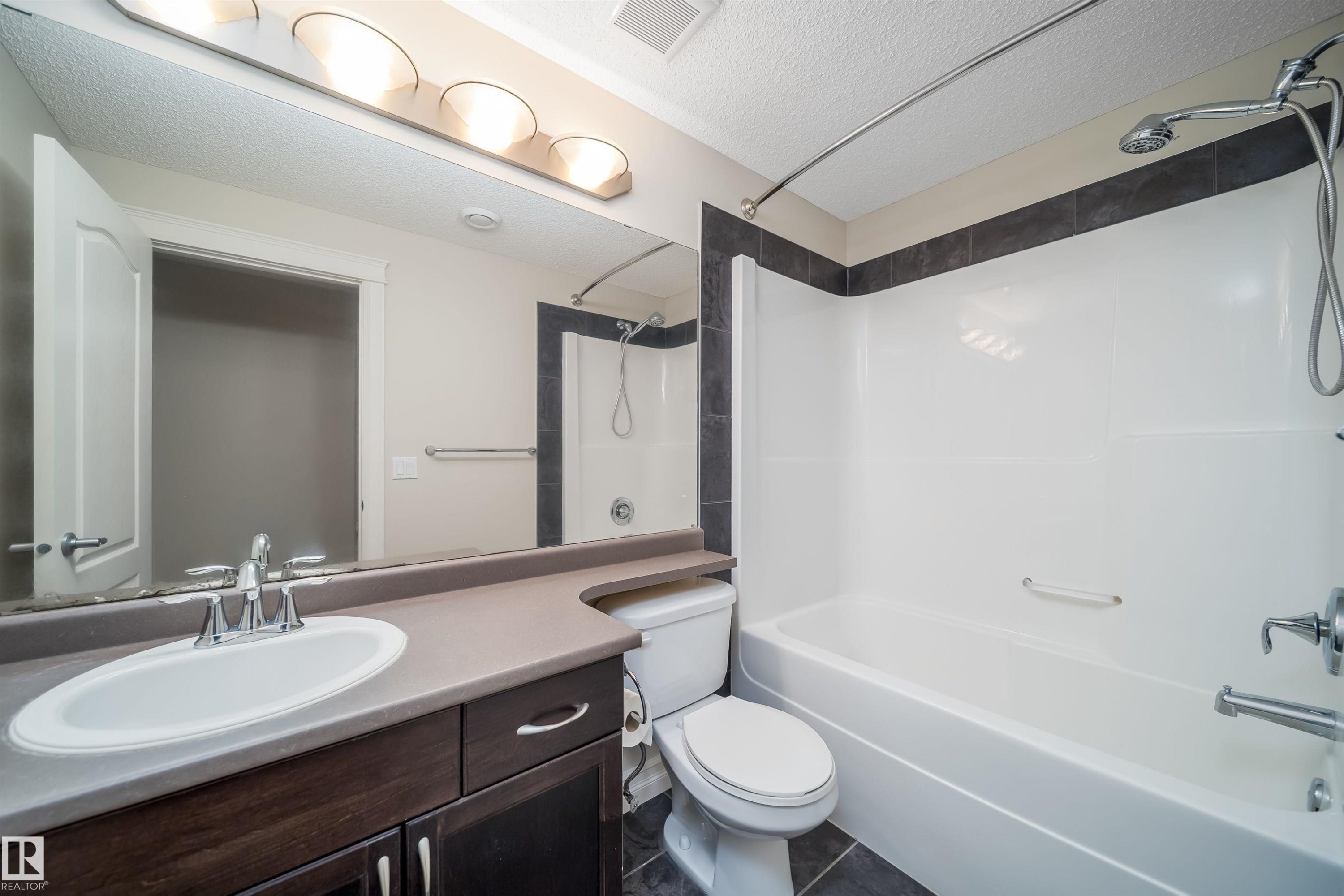 Full bathroom featuring a dark wood-finish vanity with an integrated sink, polished chrome faucet, and a large wall-mounted mirror - 11312 13 Ave Sw, Edmonton, AB