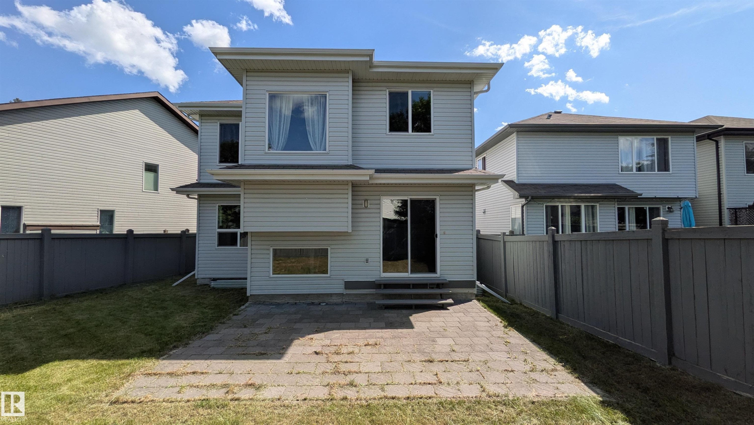 Rear exterior featuring light-colored siding, a multi-level design, and a ground-level patio with pavers - 11312 13 Ave Sw, Edmonton, AB