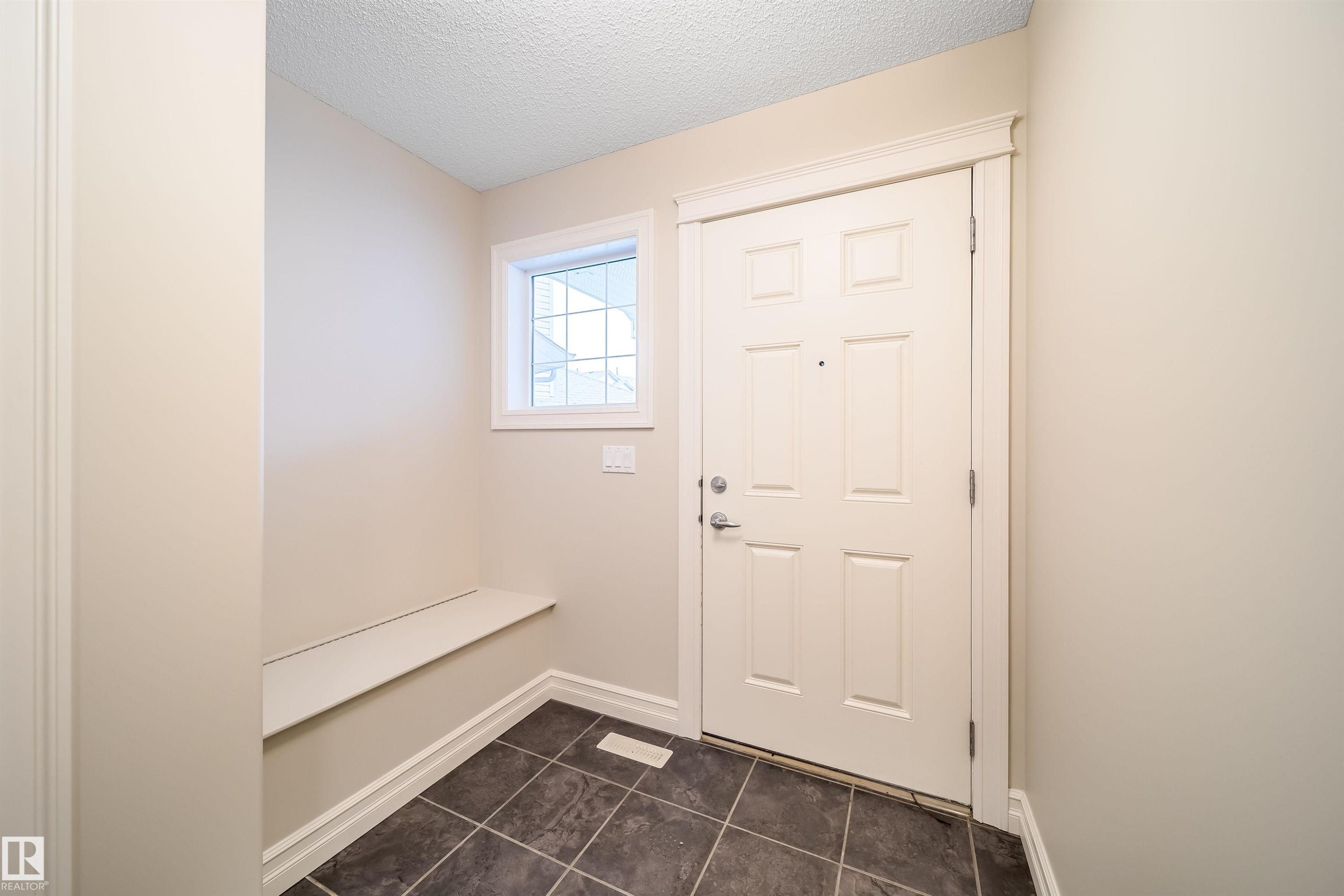 Entryway featuring a paneled door, square tile flooring, built-in bench, and a transom window - 11312 13 Ave Sw, Edmonton, AB