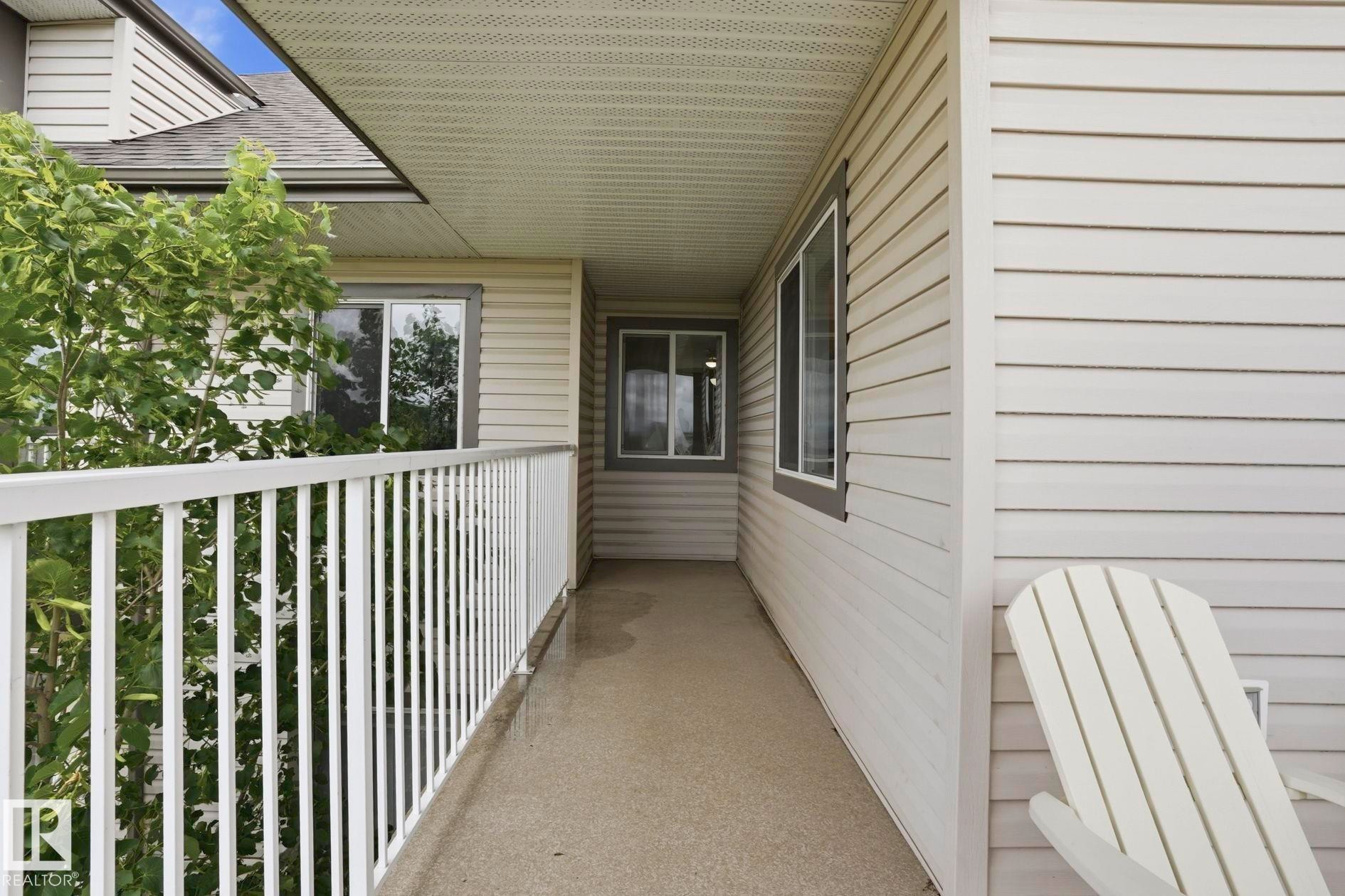 Covered outdoor balcony featuring a white railing, siding exterior, and durable concrete surface - #426 3425 19 St Nw, Edmonton, AB