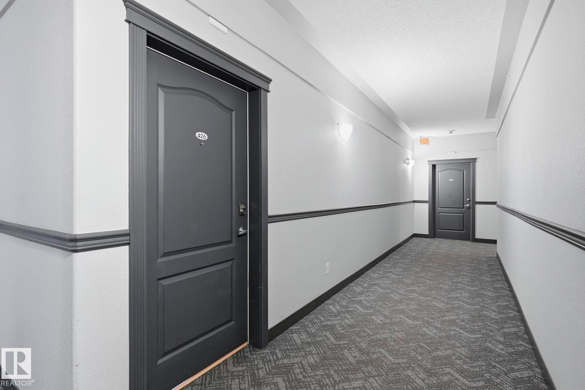 Hallway with textured gray carpeting, white walls, and dark gray wainscoting - #426 3425 19 St Nw, Edmonton, AB