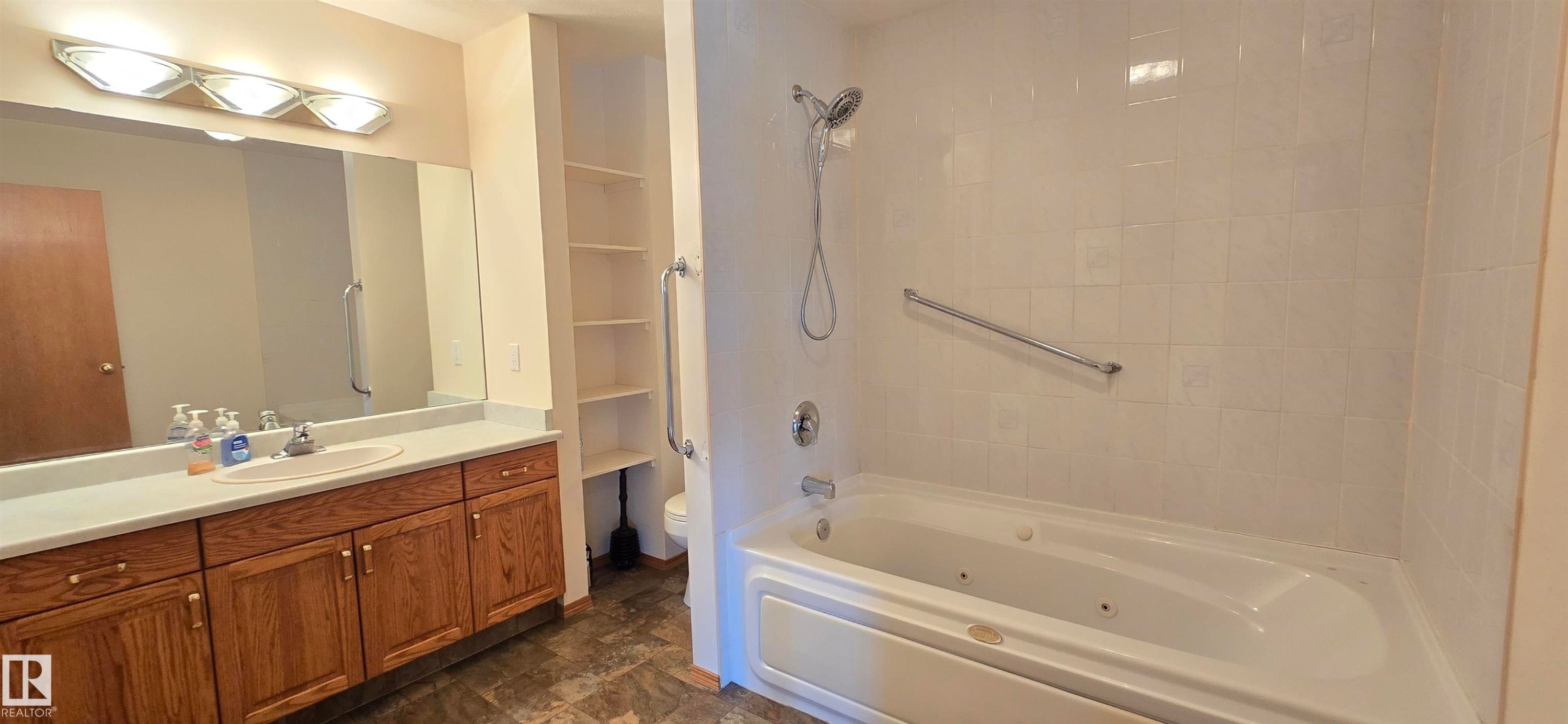 Bathroom featuring a built-in jetted tub, white subway tile surround, and a chrome shower fixture - 4519 59 Ave, Vegreville, AB