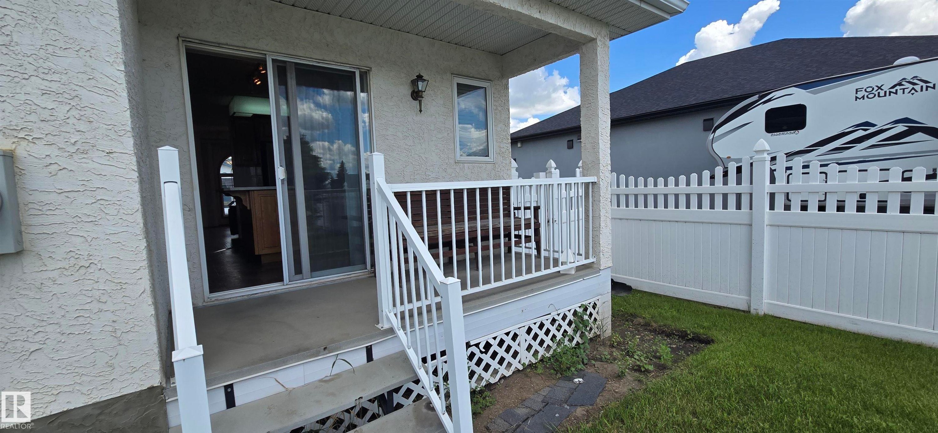 Covered patio with white railing, stucco exterior, and sliding glass door access - 4519 59 Ave, Vegreville, AB