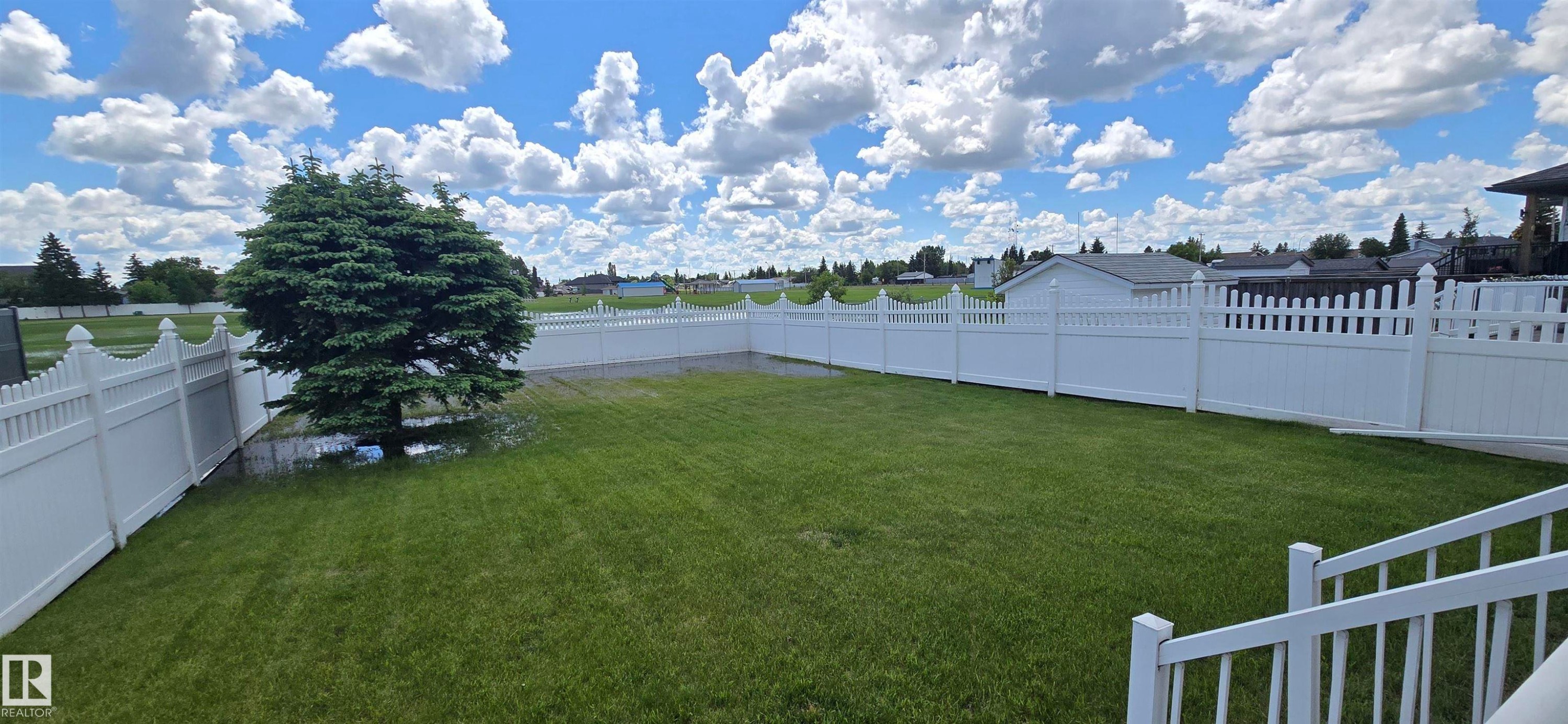 Expansive backyard featuring a mature evergreen tree, manicured lawn, full privacy fencing, and white picket fencing - 4519 59 Ave, Vegreville, AB