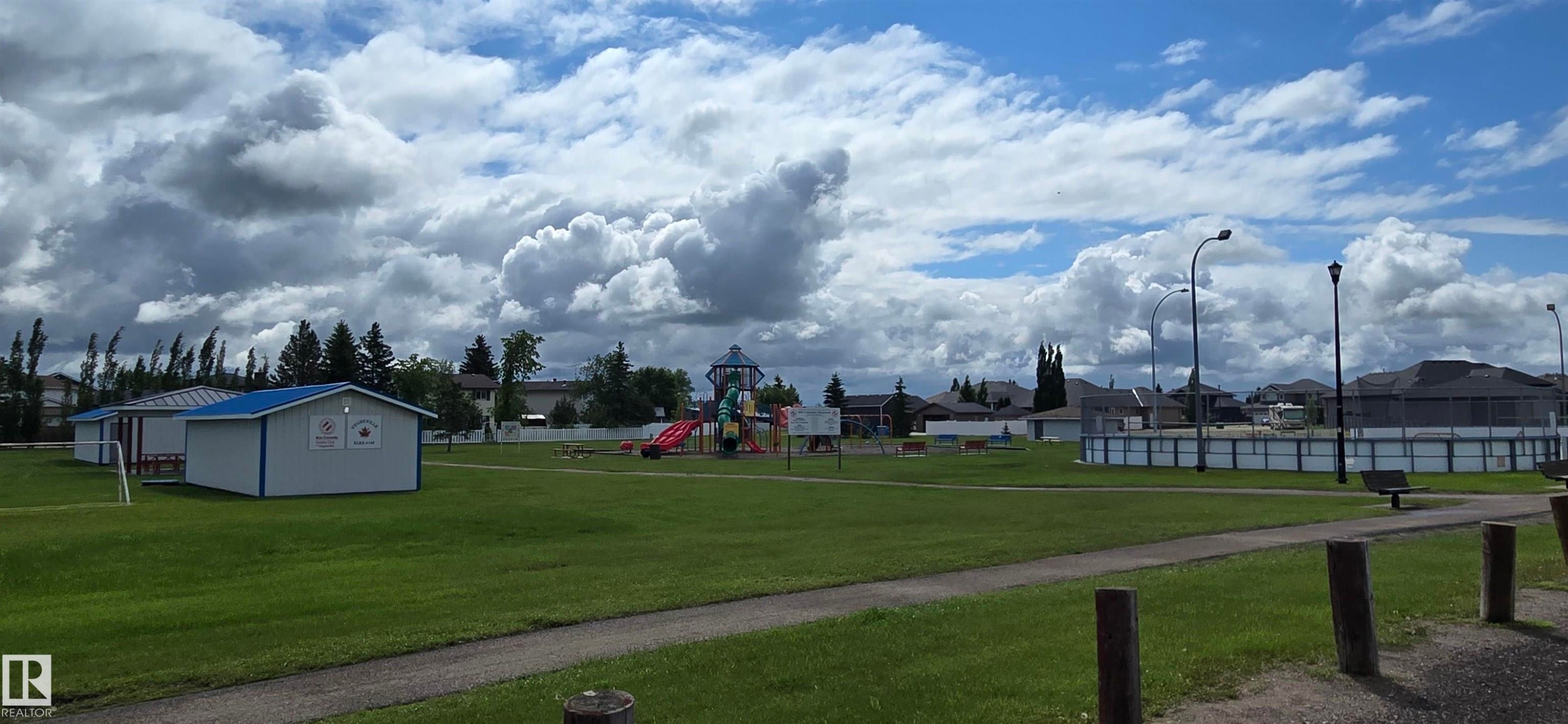 Expansive green space featuring a paved walking path, a playground, and two single-story structures with blue roofing - 4519 59 Ave, Vegreville, AB