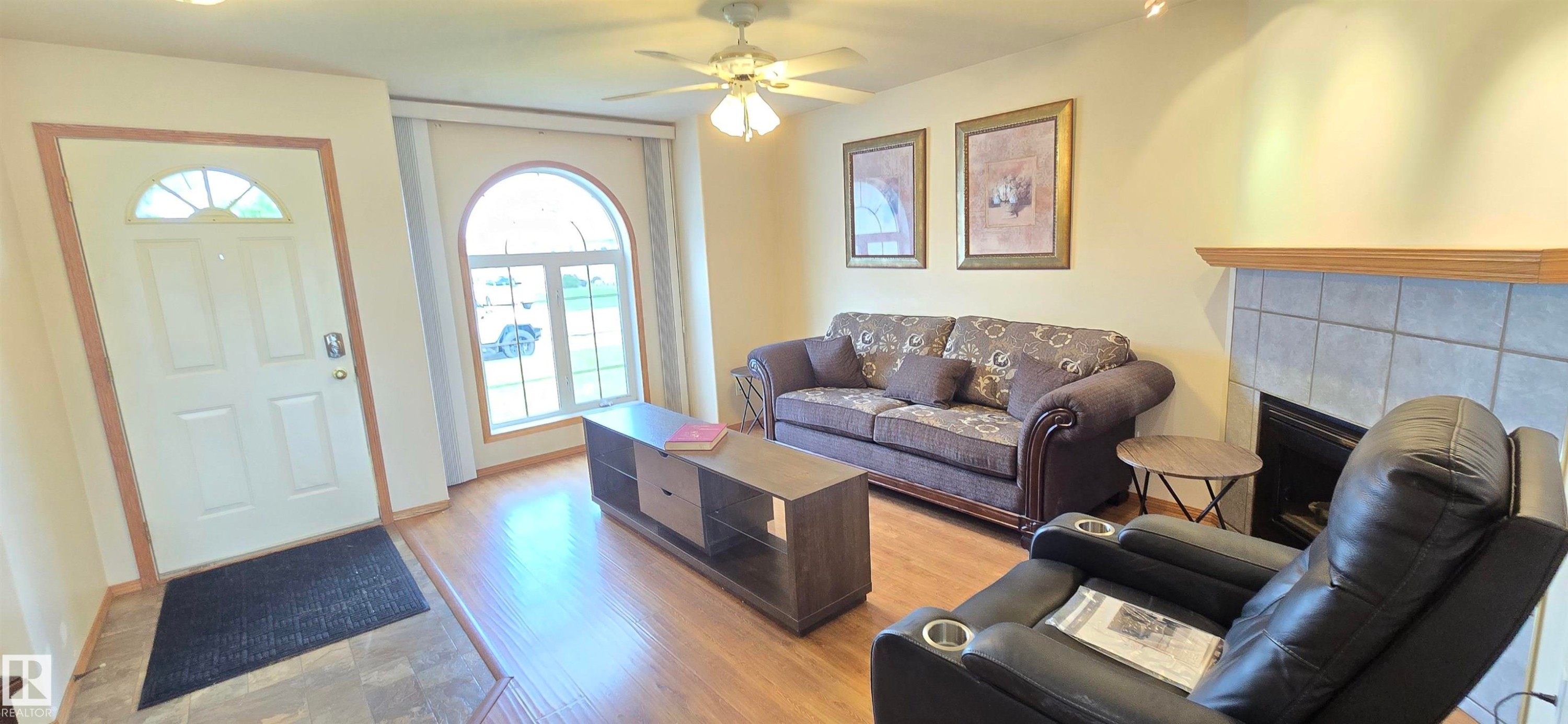 Living area featuring wood-finish flooring, a fireplace with a tile surround and wood mantel, a ceiling fan, and an arched window - 4519 59 Ave, Vegreville, AB