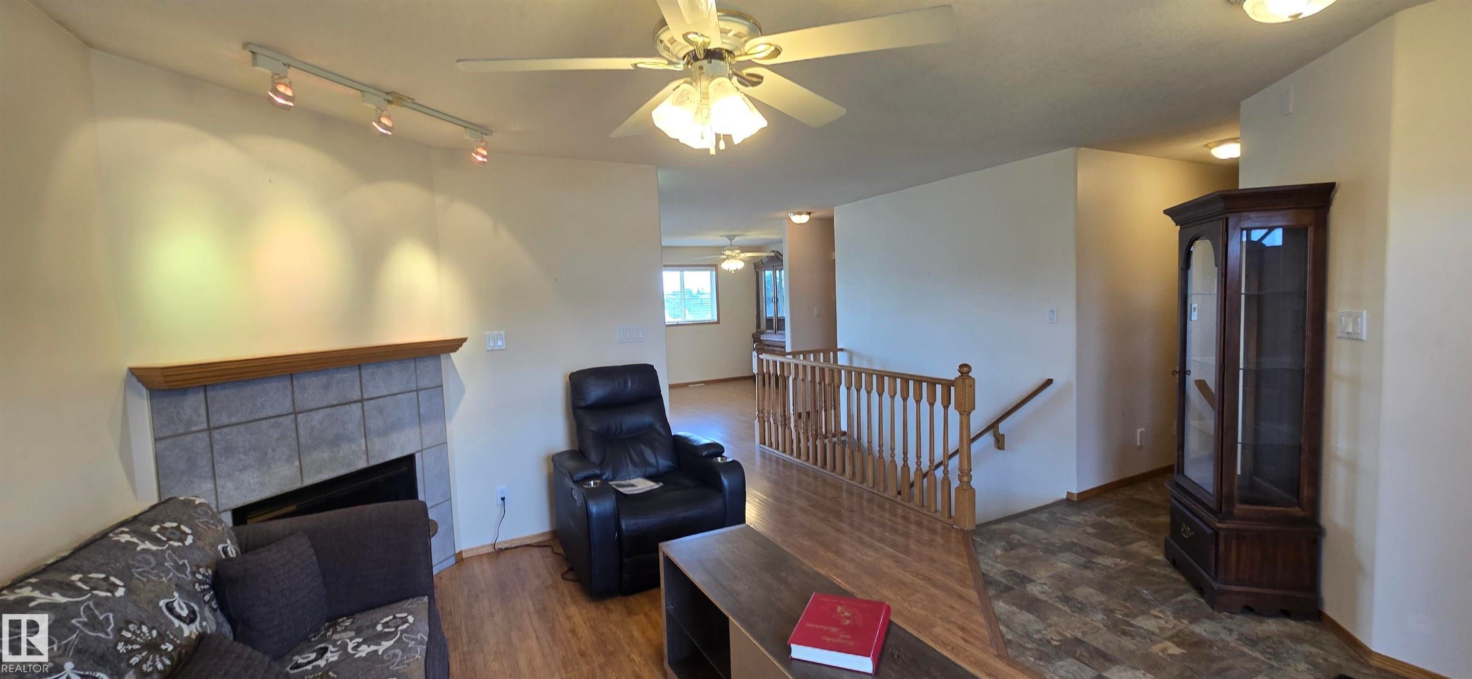 Living area featuring a tiled fireplace with wood mantel, track lighting, and a ceiling fan with integrated lighting - 4519 59 Ave, Vegreville, AB