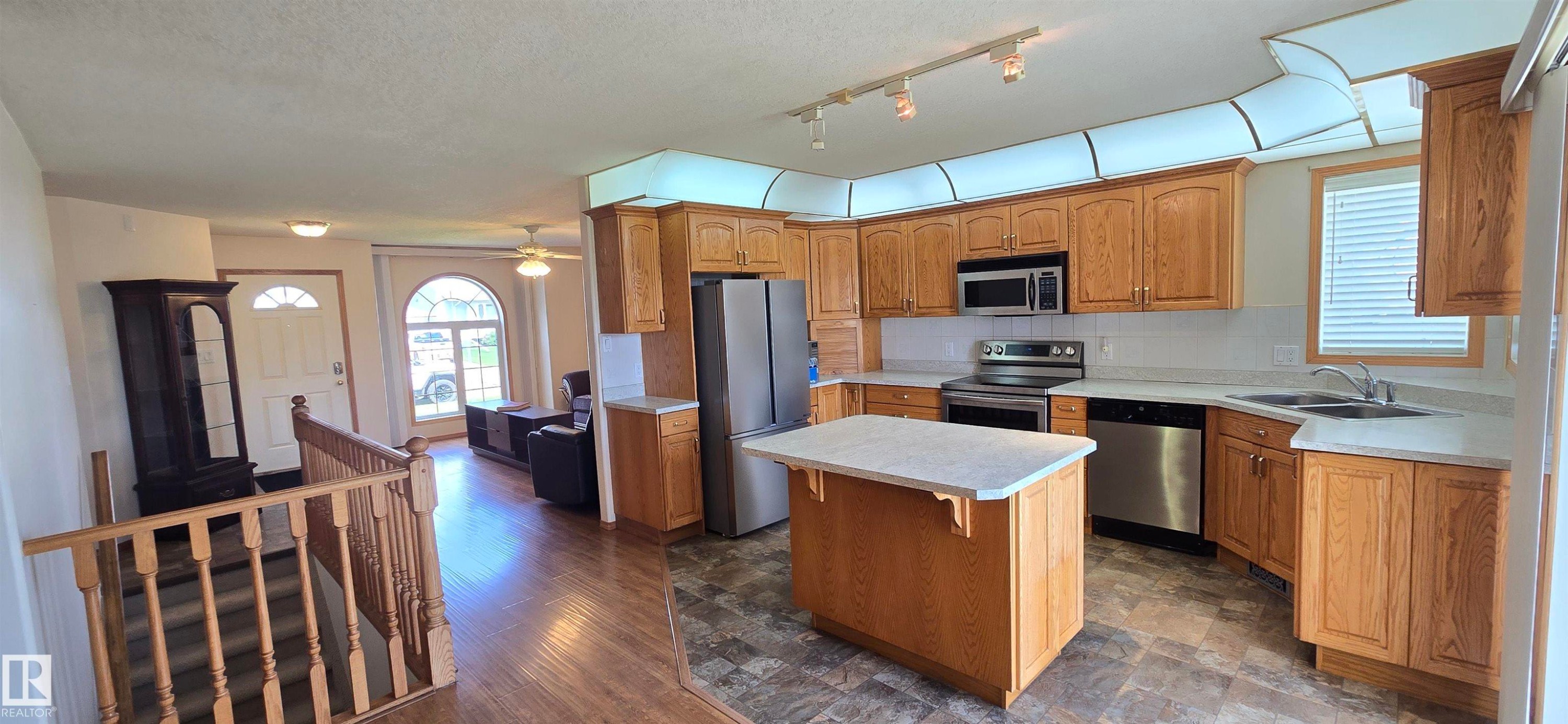 Kitchen featuring oak cabinetry, light-toned countertops, stainless steel appliances, and a central island - 4519 59 Ave, Vegreville, AB