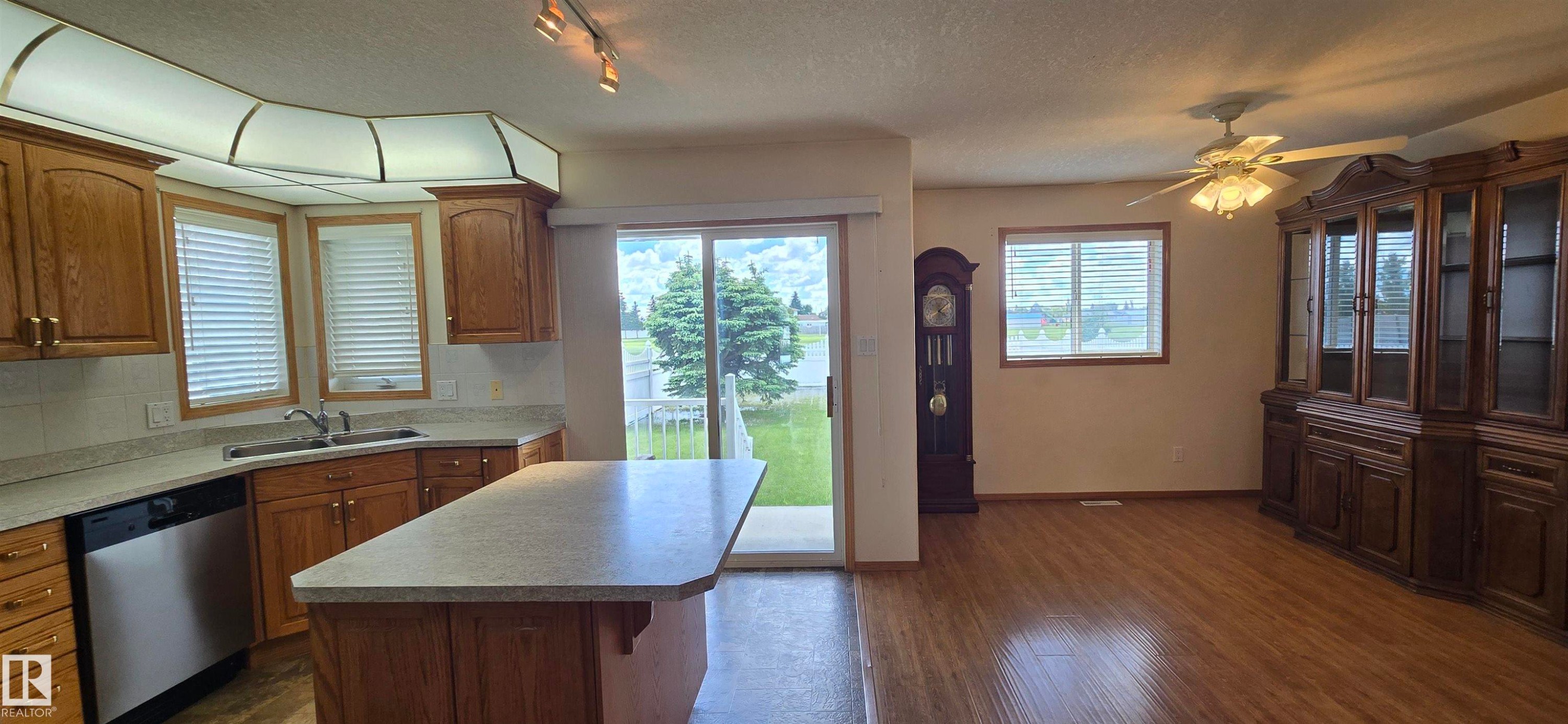 Kitchen featuring wood cabinetry, stainless steel dishwasher, and a center island with countertop seating - 4519 59 Ave, Vegreville, AB