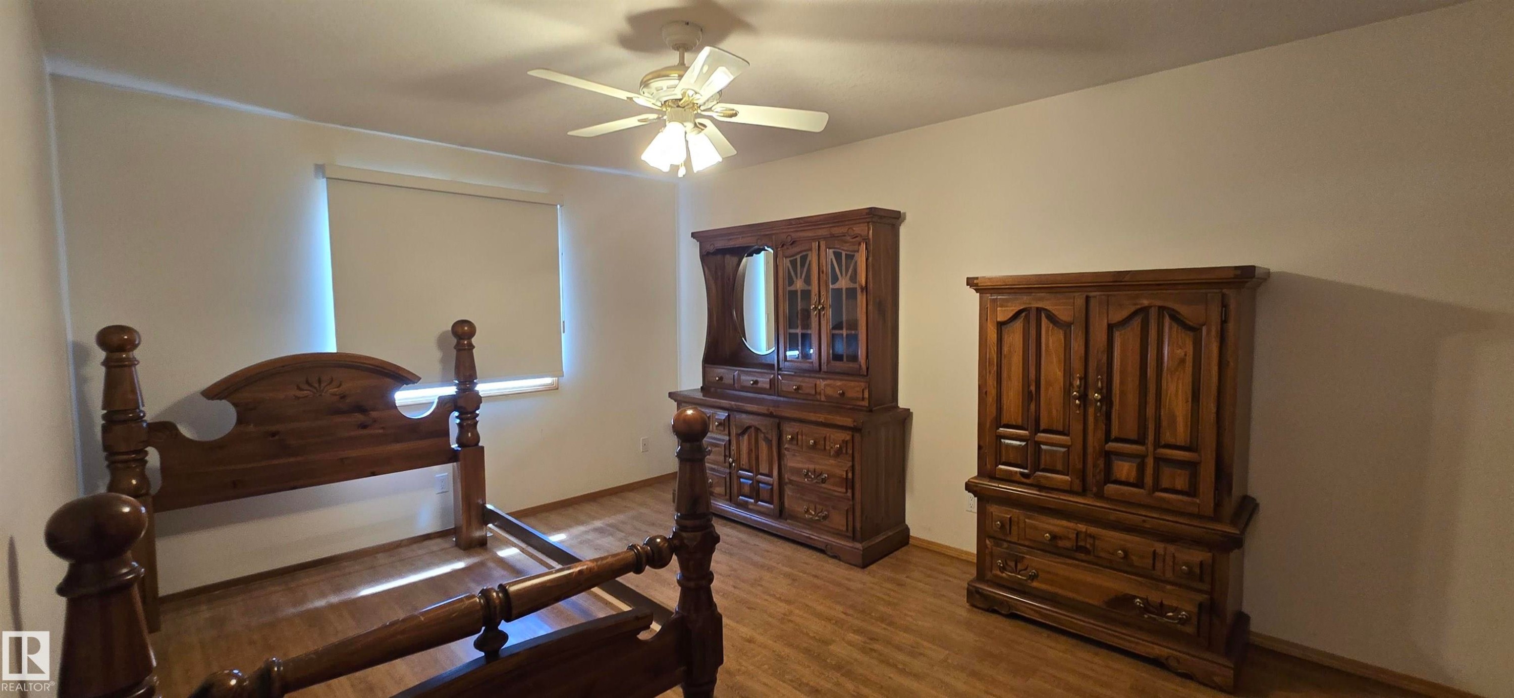 Room featuring wood-finish flooring, a ceiling fan with integrated lighting, and a window with a roller shade - 4519 59 Ave, Vegreville, AB