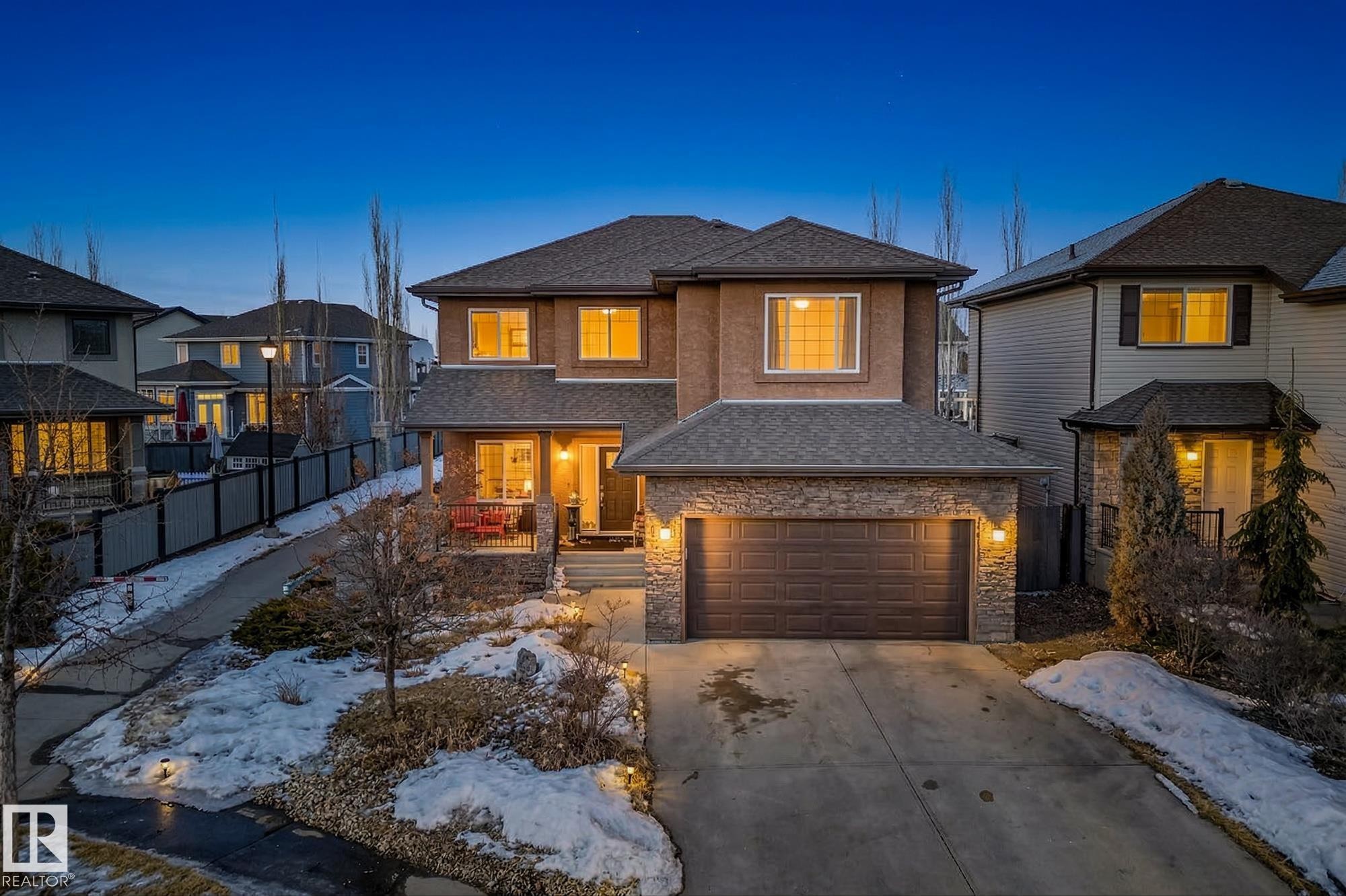 View of front of property featuring roof with shingles, stone siding, driveway, a garage, and a porch - 1660 Malone Way, Edmonton, AB