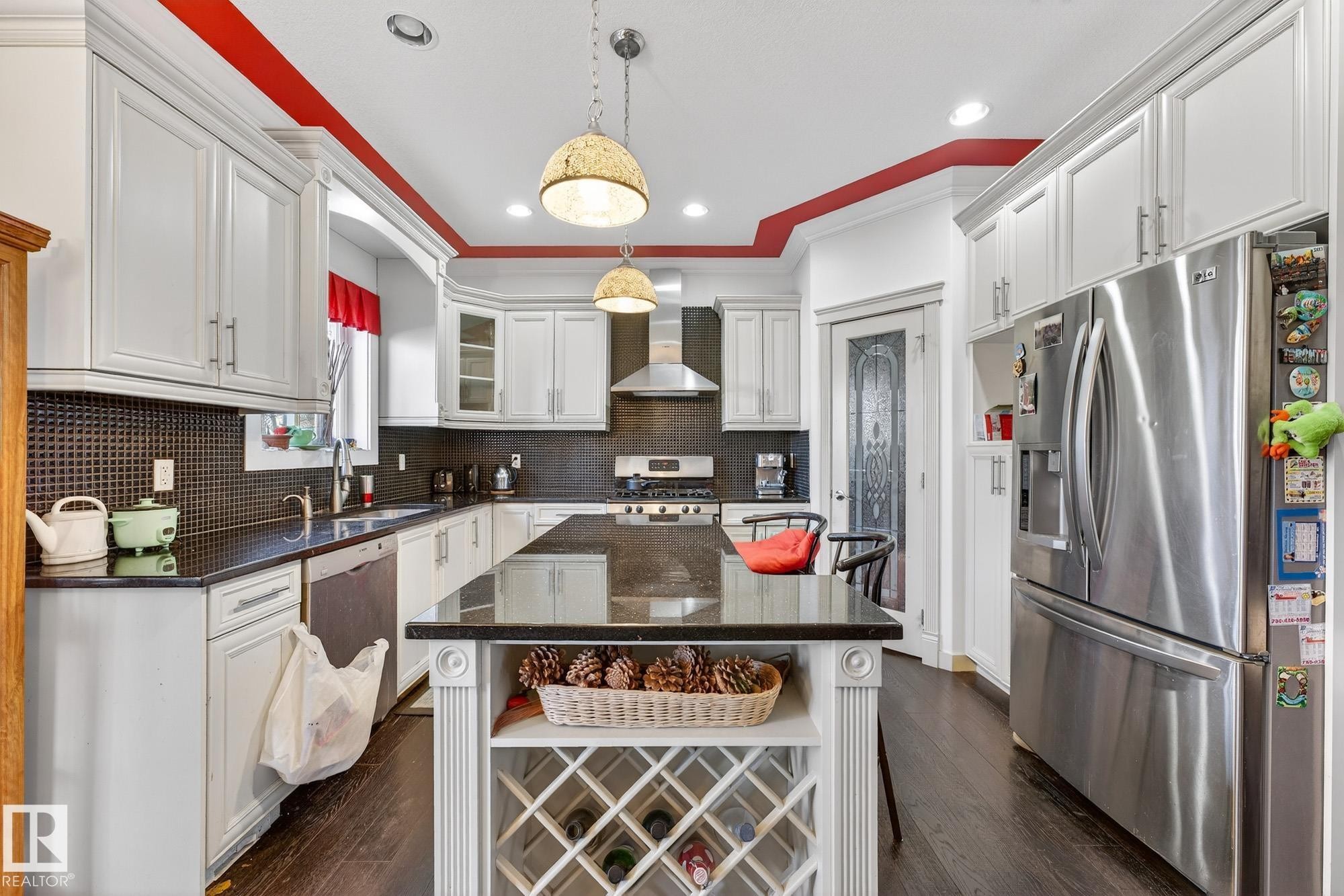 Kitchen featuring stainless steel appliances, dark stone countertops, dark wood-style floors, white cabinetry, and crown molding - 1660 Malone Way, Edmonton, AB