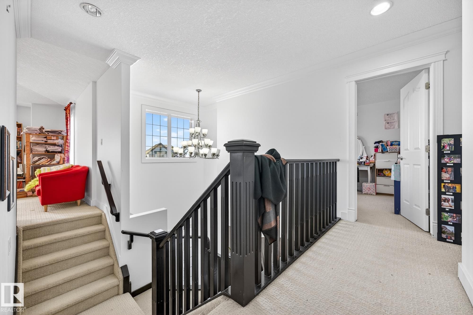 Hallway with an upstairs landing, light carpet, hanging lights, a textured ceiling, and crown molding - 1660 Malone Way, Edmonton, AB