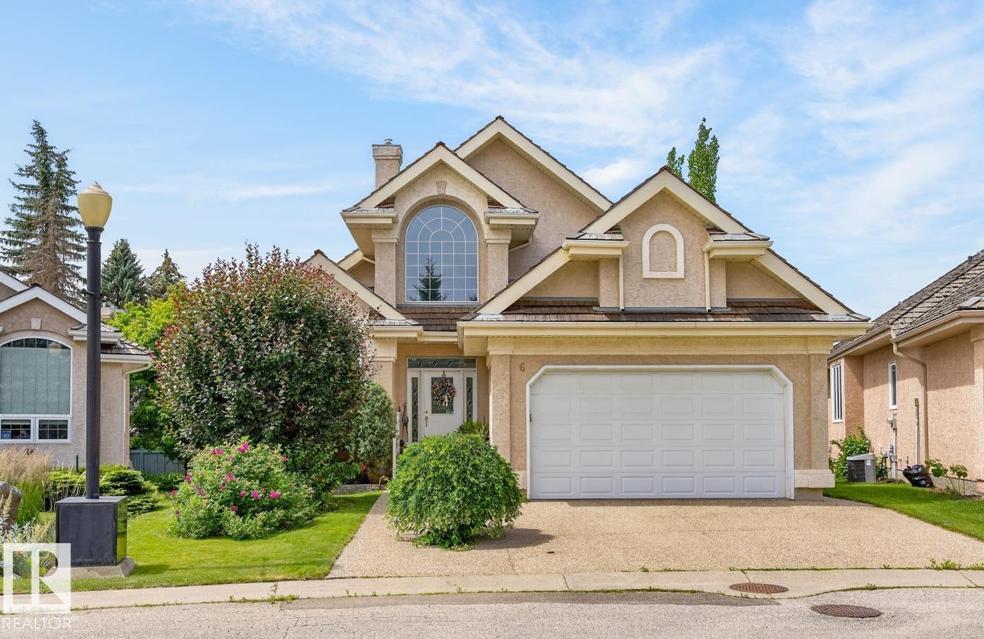 Stucco exterior with a pitched roofline, featuring an arched window, a two-car garage, and a concrete driveway - 6 Prestige Point Nw, Edmonton, AB