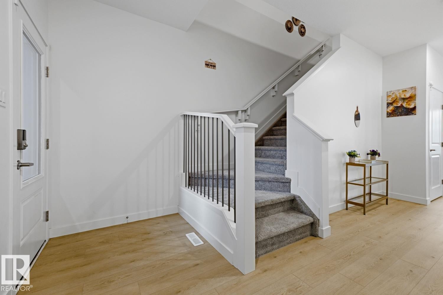 Entryway featuring light wood-finish flooring, white walls, and a staircase with carpeted treads and a white newel post and railings with black spindles - 22924 82 Ave Nw, Edmonton, AB - Indoor Photo Showing Other Room