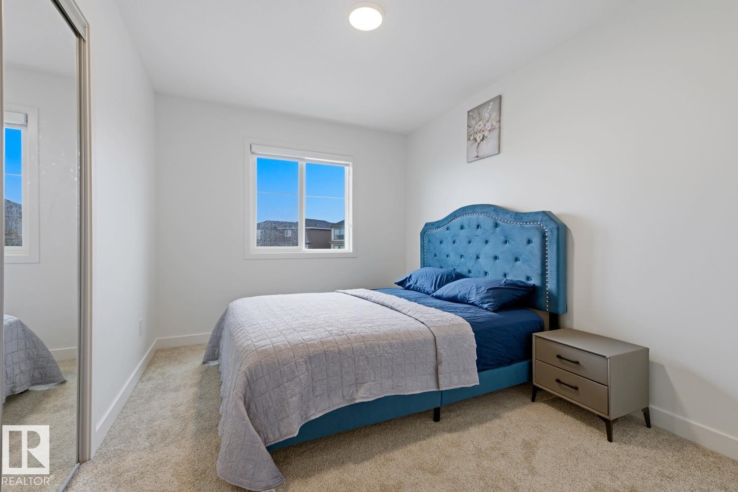 Spacious bedroom featuring light neutral wall paint, plush carpet flooring, a large window, and a mirrored sliding closet door - 22924 82 Ave Nw, Edmonton, AB - Indoor Photo Showing Bedroom
