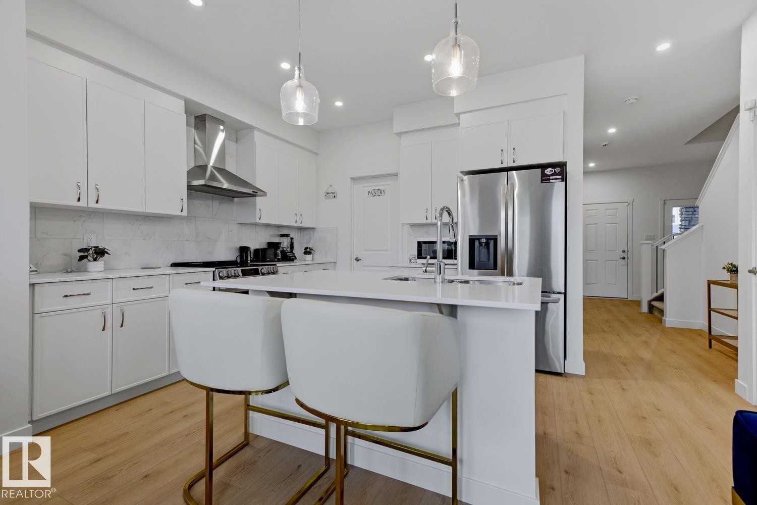 Modern kitchen featuring white cabinetry, a stone countertop island with seating, stainless steel appliances, and wood-finish flooring - 22924 82 Ave Nw, Edmonton, AB - Indoor Photo Showing Kitchen With Upgraded Kitchen