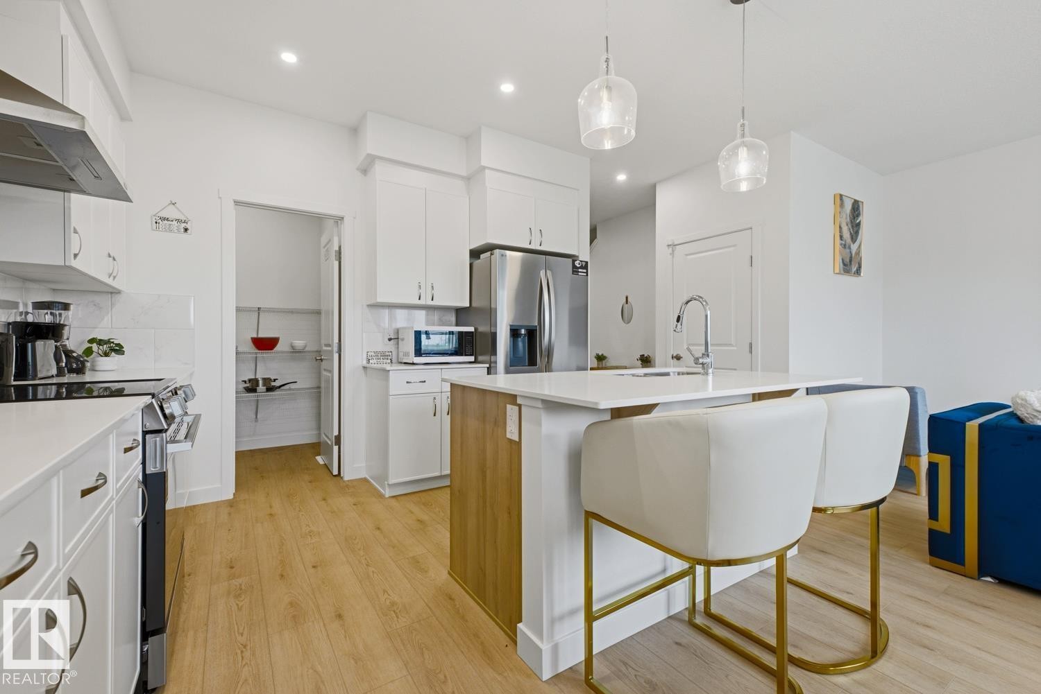 Contemporary kitchen featuring white cabinetry, light wood-finish flooring, stainless steel appliances, a center island with seating, and a pantry with wire shelving - 22924 82 Ave Nw, Edmonton, AB - Indoor Photo Showing Kitchen With Upgraded Kitchen