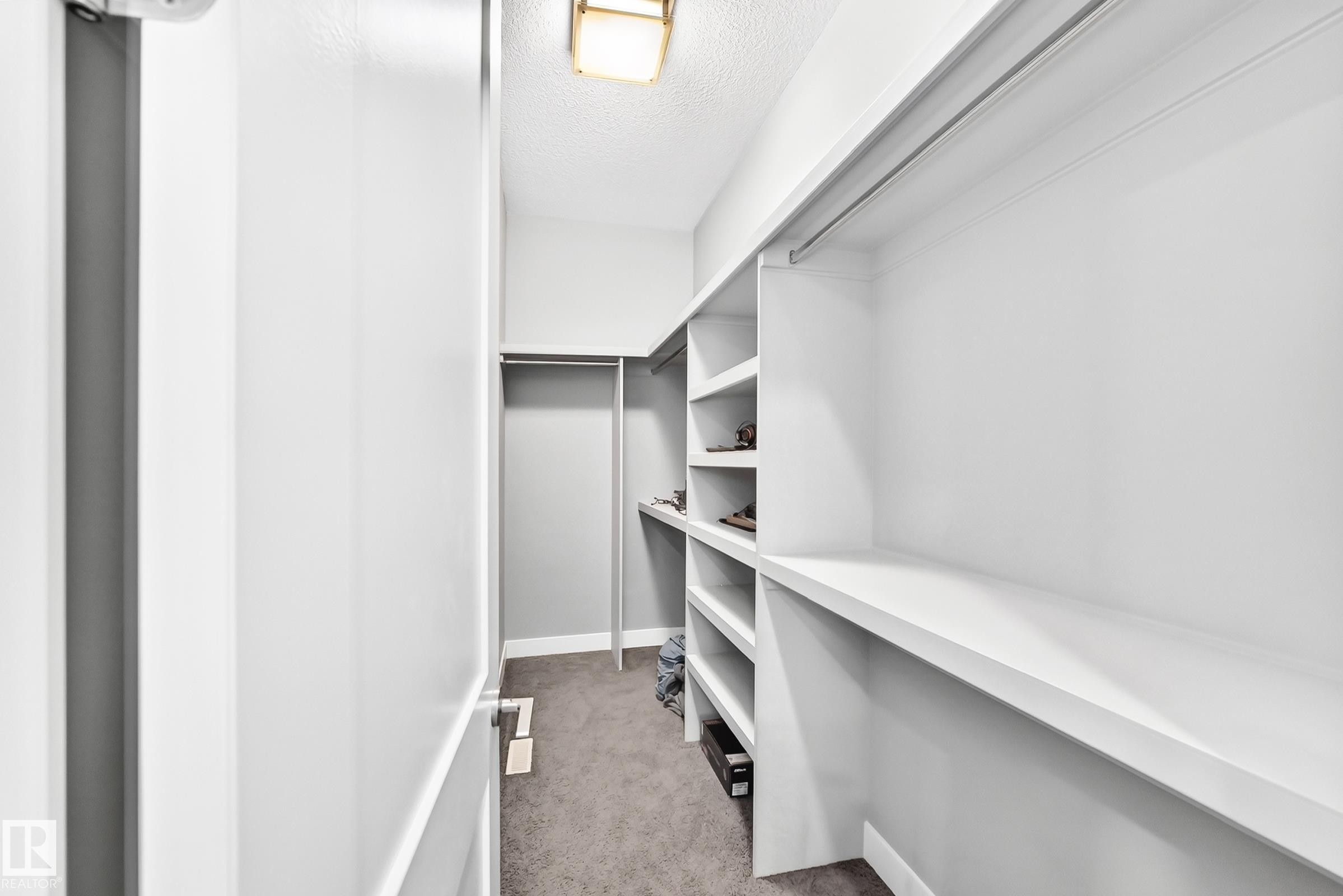 Walk-in closet featuring white built-in shelving, hanging rods, and grey carpeting - 1781 Melrose Crescent, Edmonton, AB