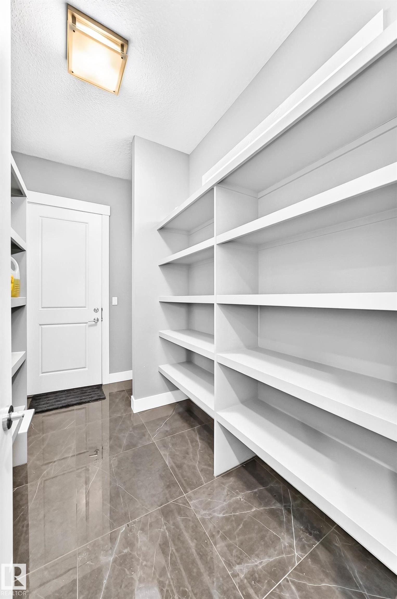 Spacious pantry featuring extensive built-in shelving, durable tile flooring, a solid panel interior door, and a flush-mount ceiling light fixture - 1781 Melrose Crescent, Edmonton, AB